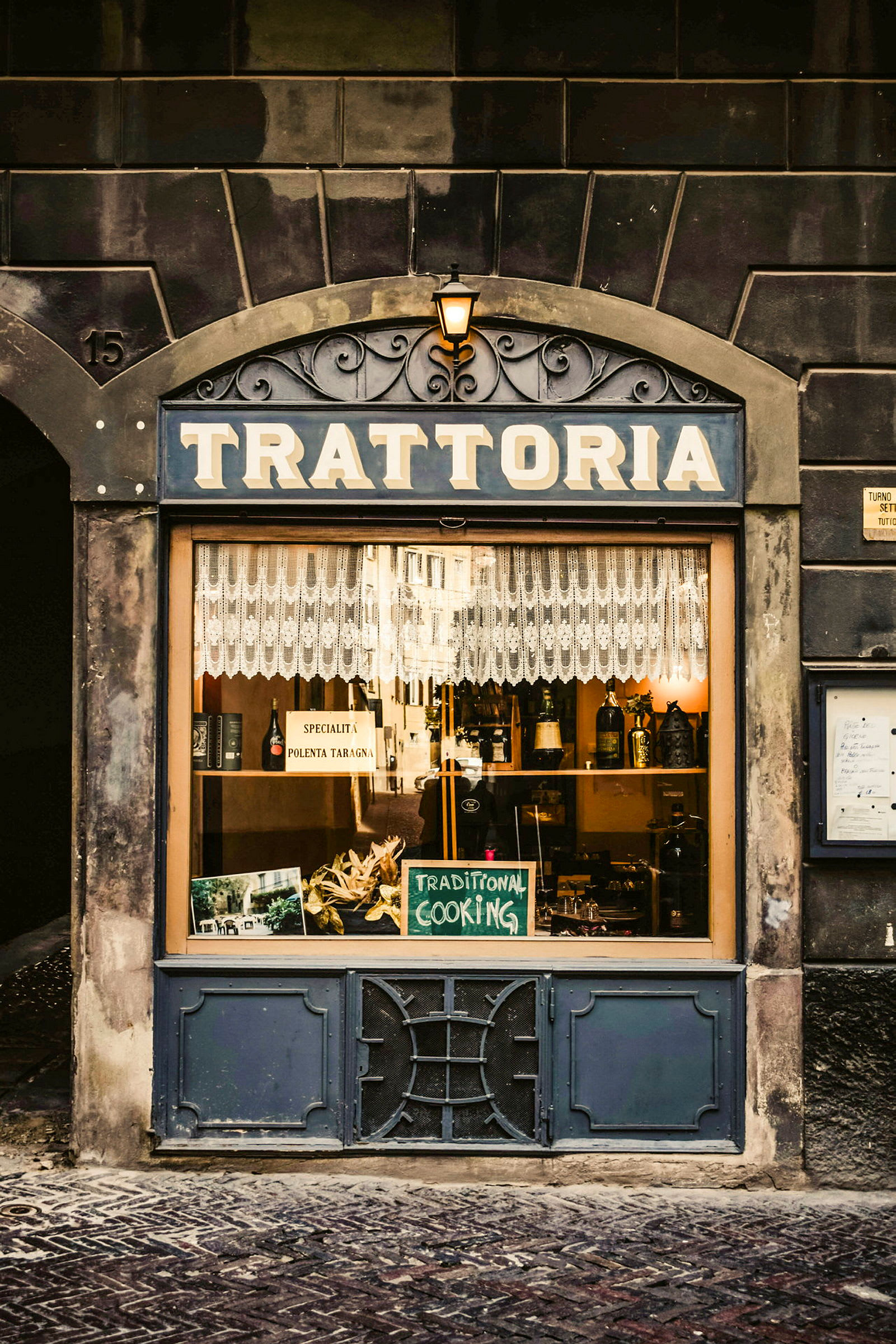 Et vindue til en trattoria med et skilt der står 'Traditional Cooking' og bordpynt. (AI-genereret tekst)