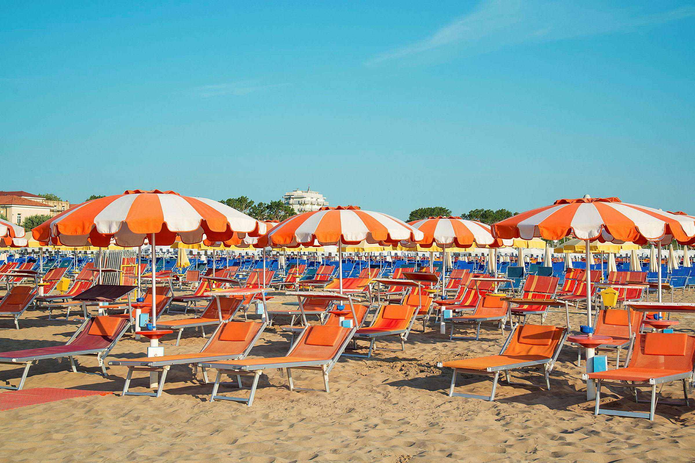 Billede af en sandstrand med orange og hvide parasoller samt liggestole. (AI-genereret tekst)