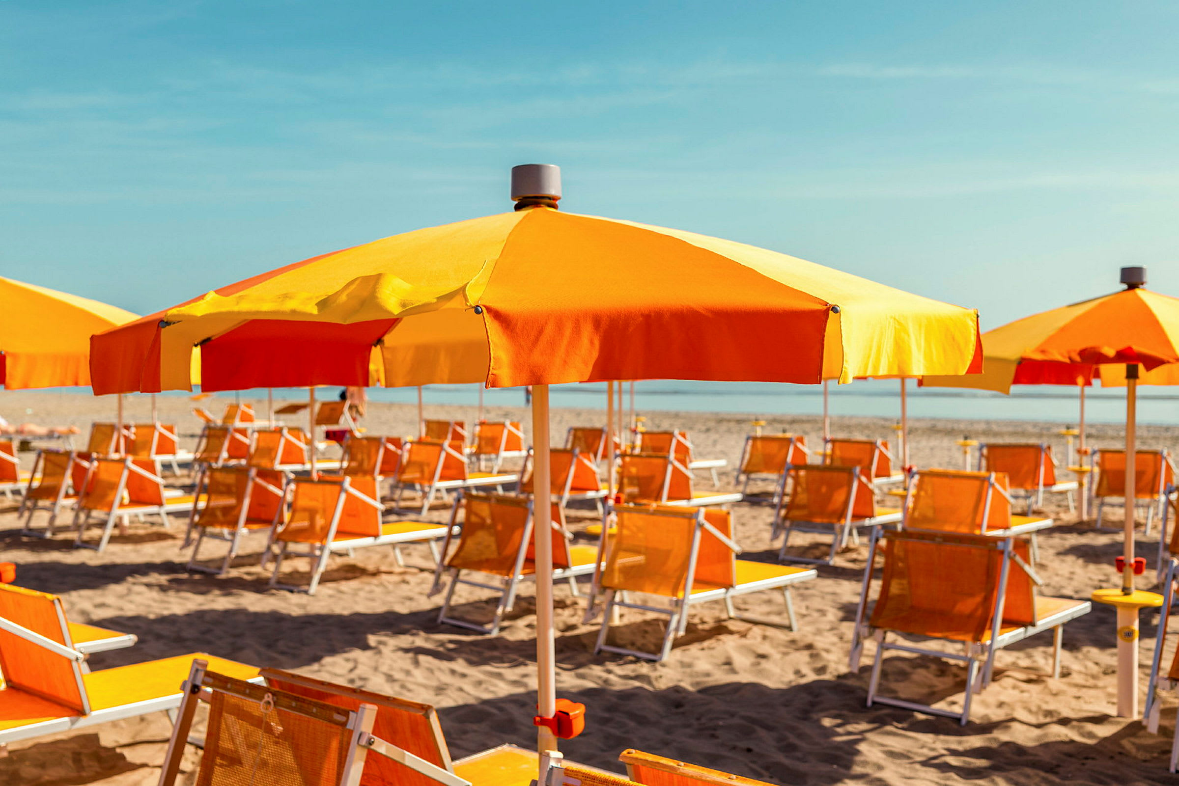 Solsenge og parasoller i orange og gul står på en sandstrand. (AI-genereret tekst)