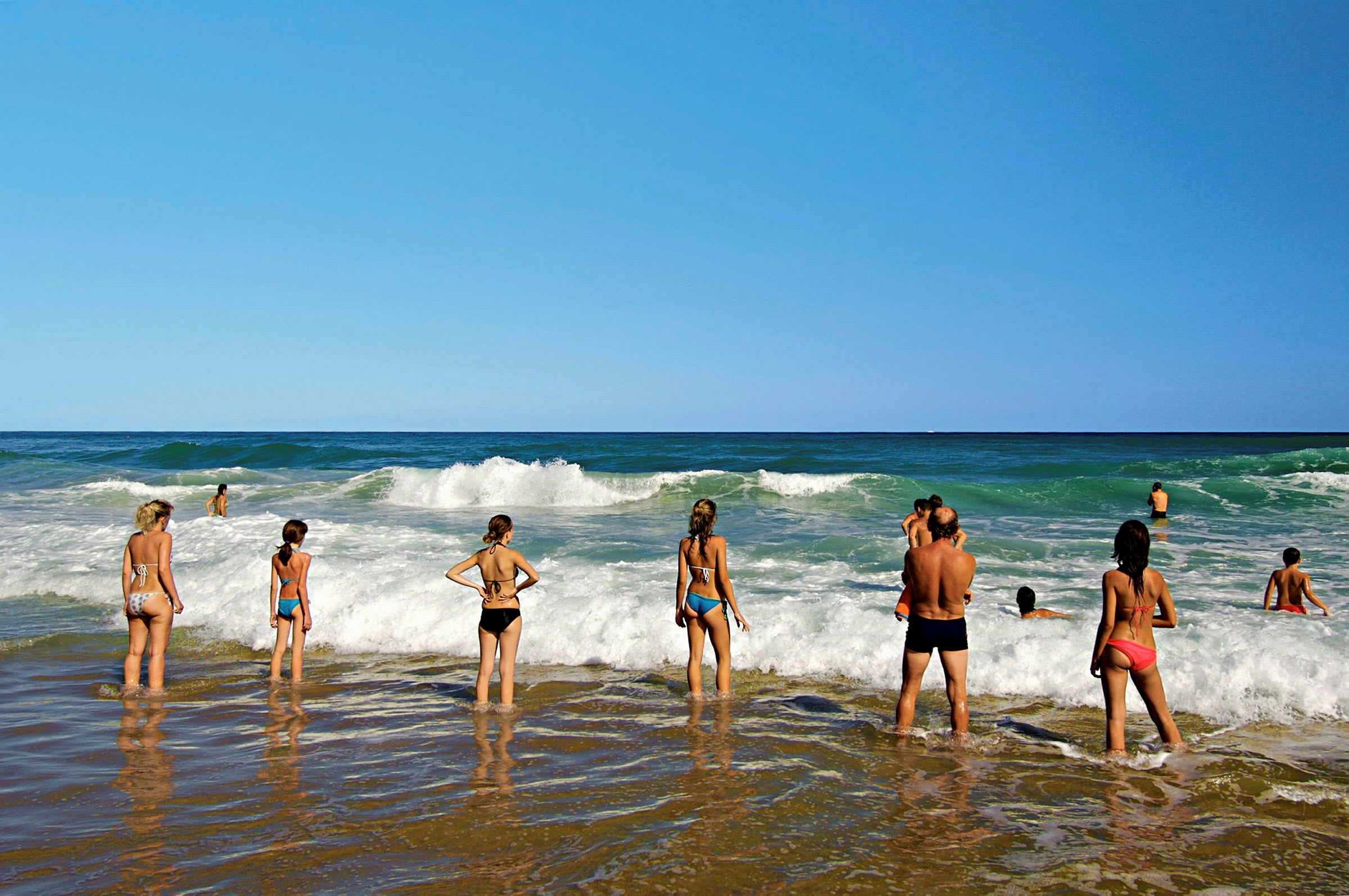 Mennesker står på en strand og kigger ud over bølgerne i havet. (AI-genereret tekst)