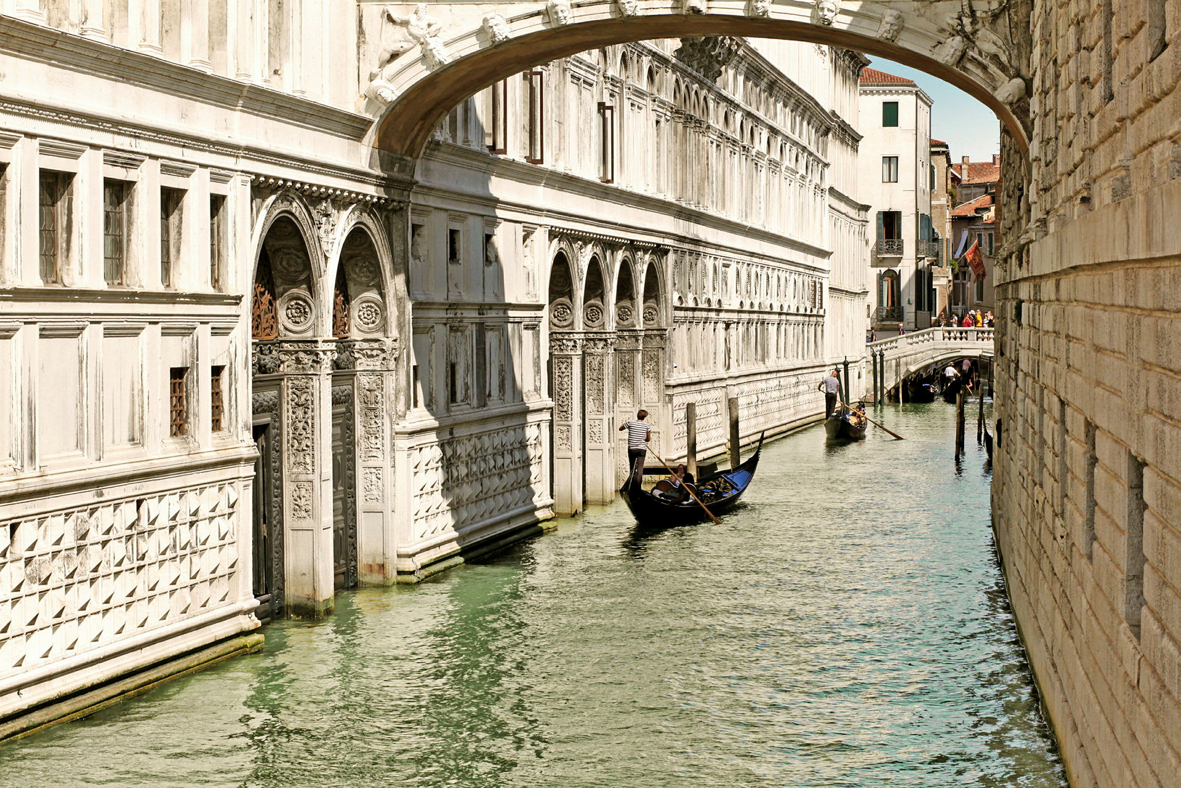 En gondol bevæger sig langs en kanal i Venedig, omgivet af historiske bygninger og en lille bro. (AI-genereret tekst)