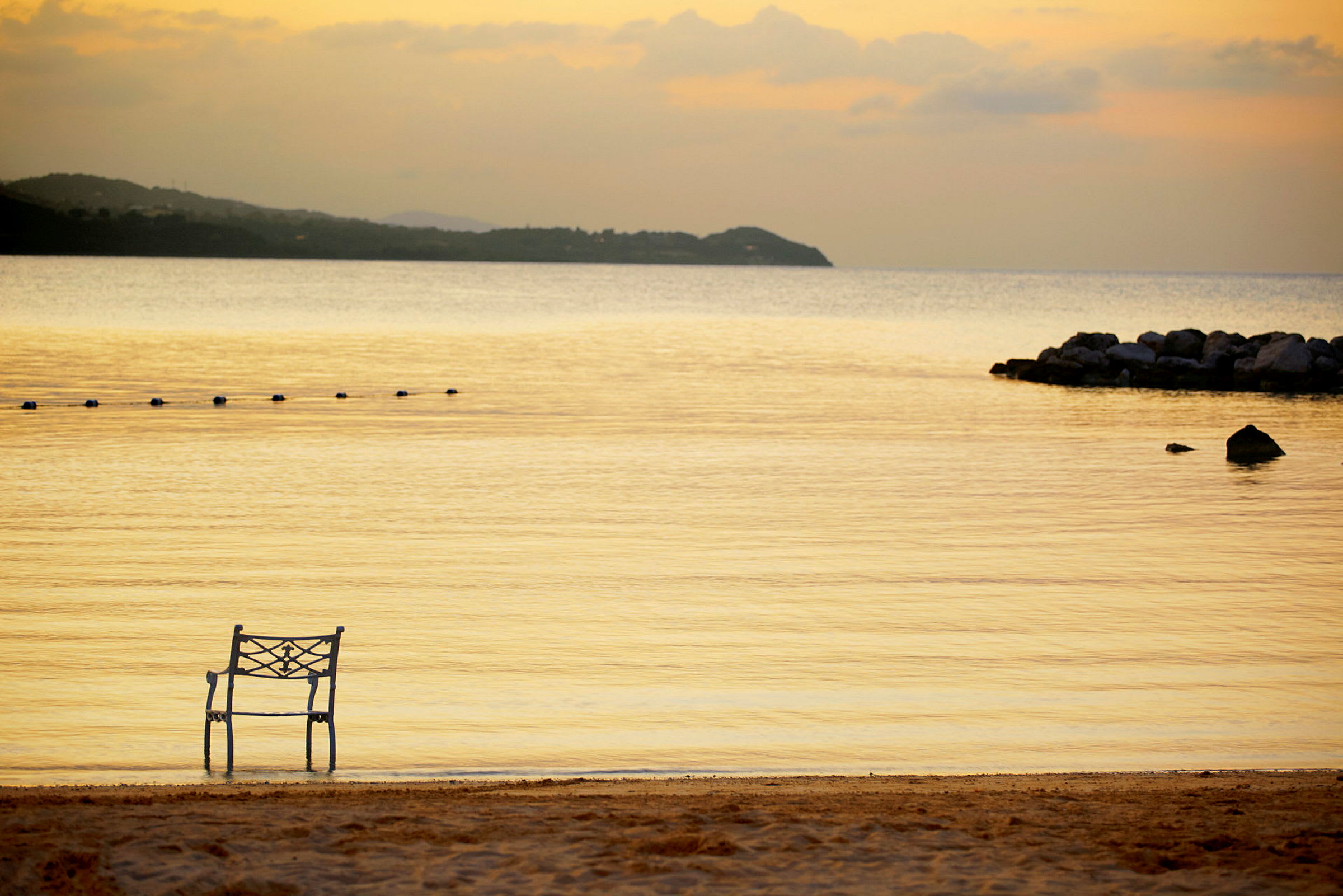 En stol placeret ved stranden med stille vand og en solnedgang i baggrunden. (AI-genereret tekst)