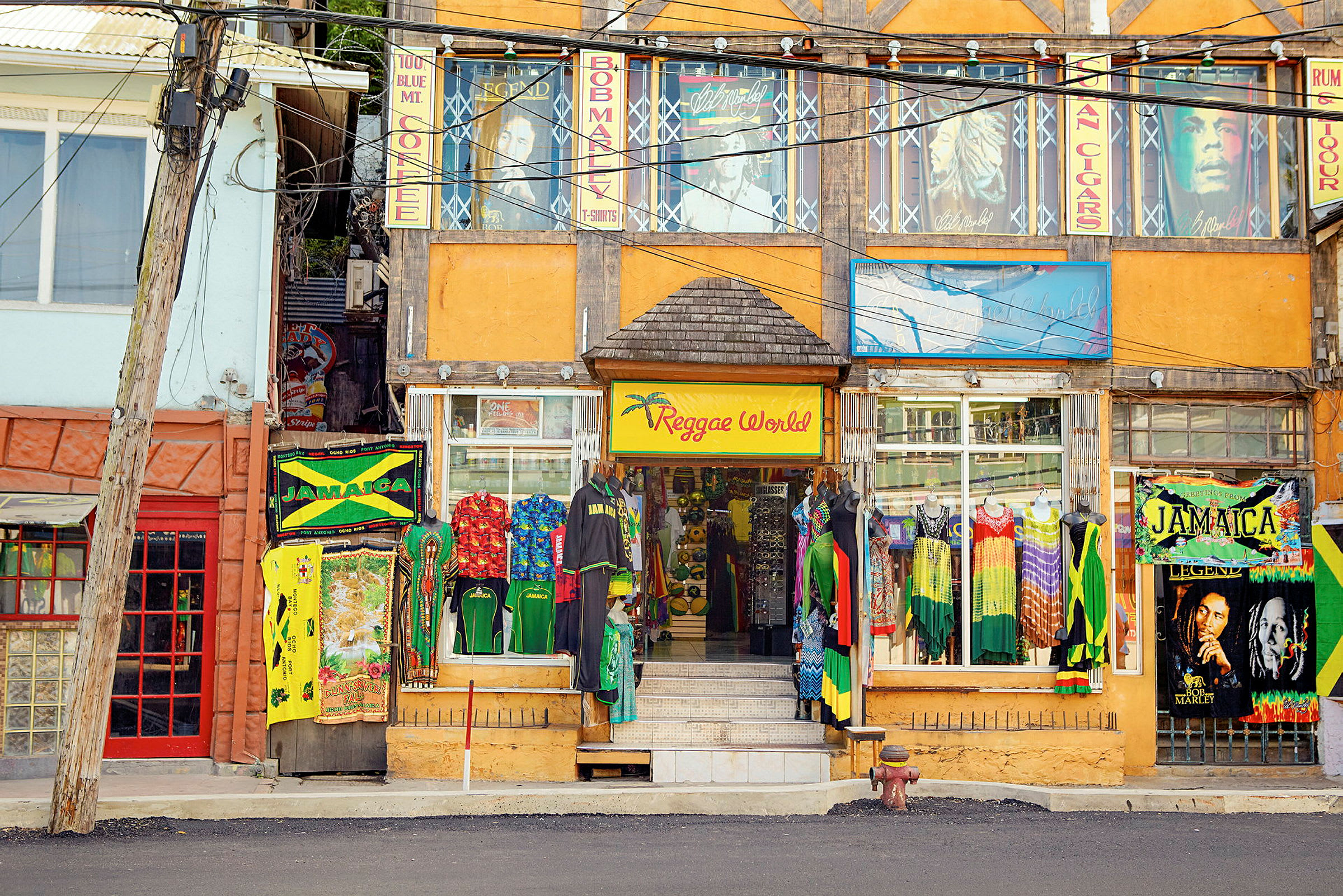 En farverig butik med reggae-tema ligger ved en gade, med tøj og skilte inspireret af Jamaica. (AI-genereret tekst)