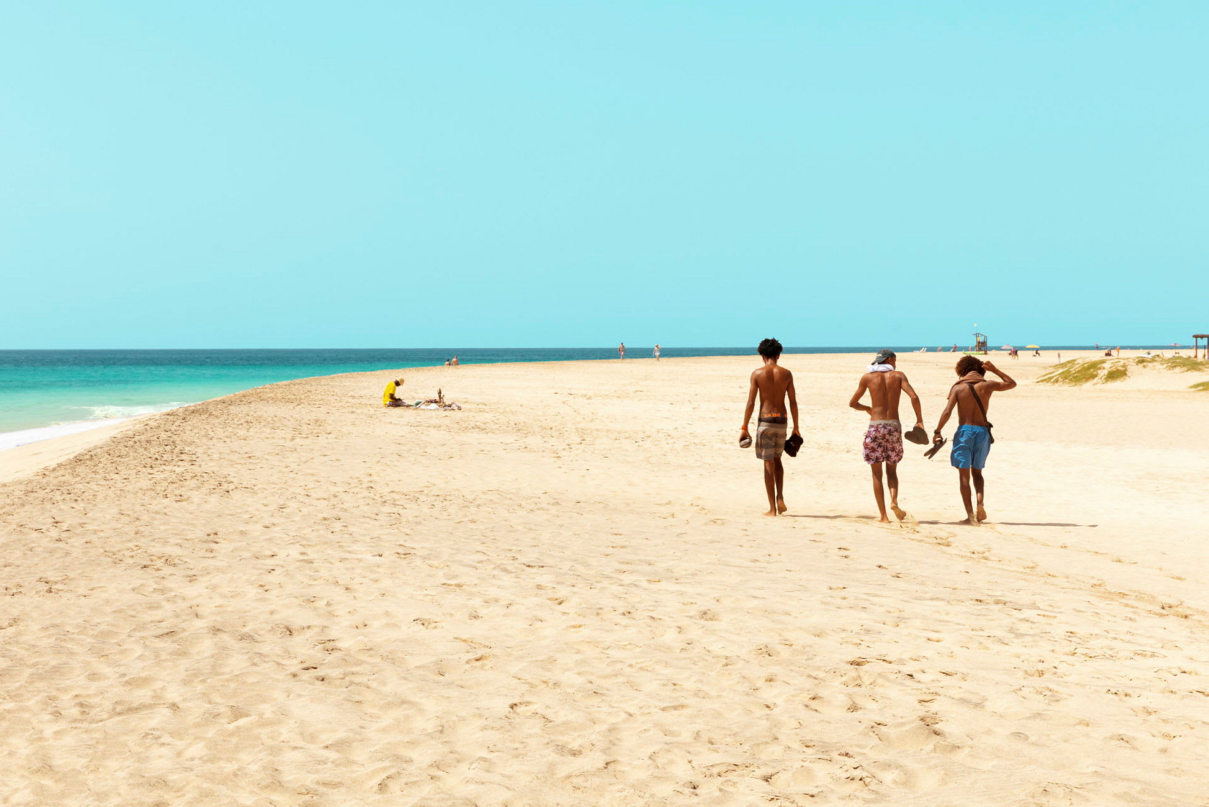 Tre personer går på en sandstrand tæt ved havet. (AI-genereret tekst)