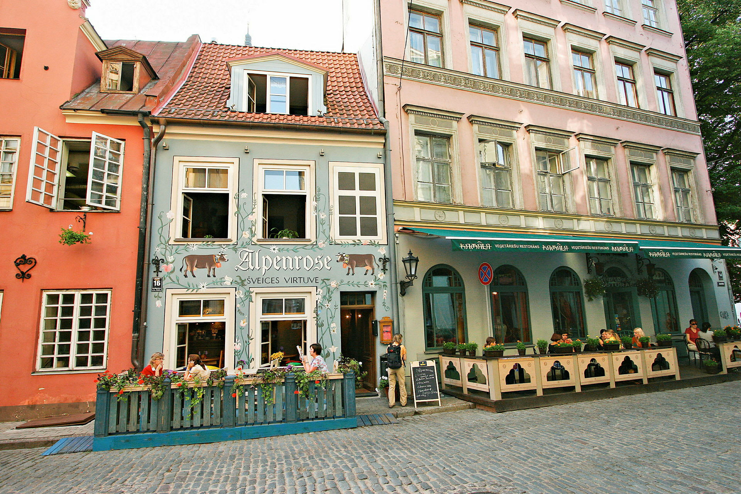 Farverige historiske bygninger med restauranter og caféer, og mennesker der sidder udenfor ved bordene. (AI-genereret tekst)