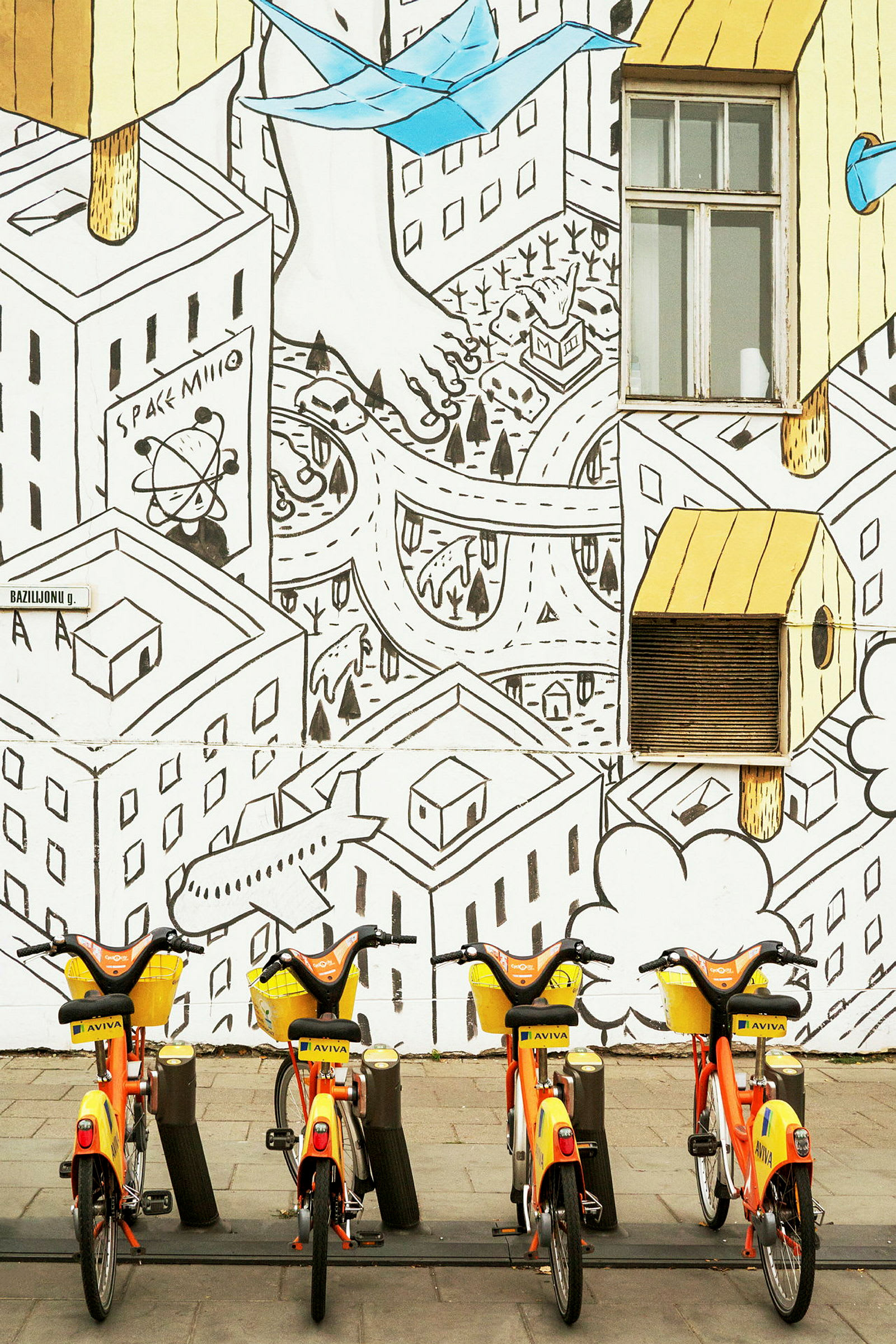 En række gule og orange cykler foran en væg med illustreret bylandskab. (AI-genereret tekst)