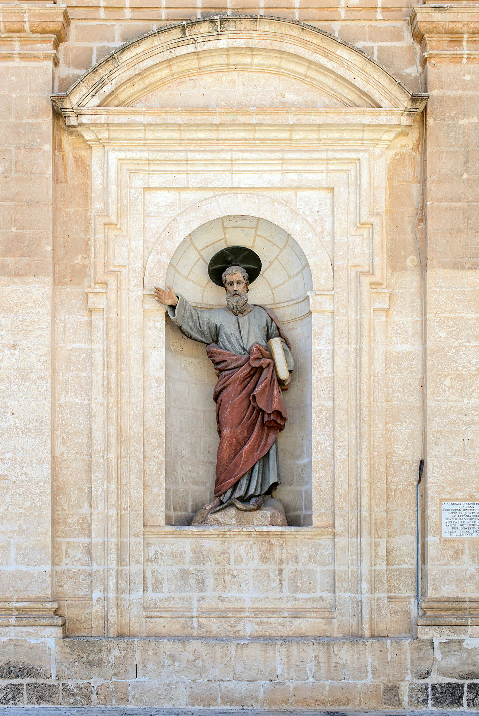 Statue af en person i traditionelle klæder, placeret i en niche på en stenbygning. (AI-genereret tekst)