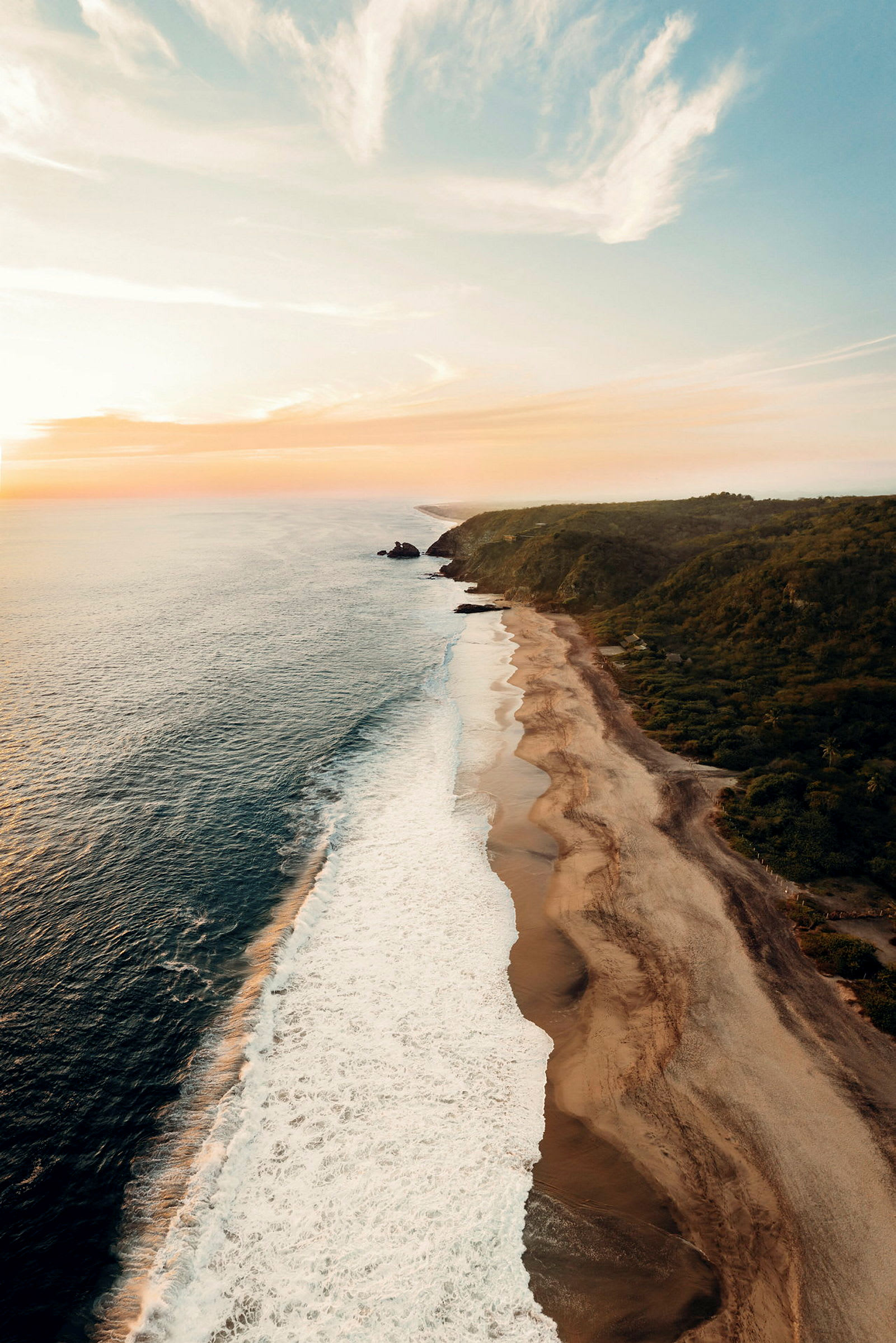 En kystlinje med en bred strand, der møder bølgerne fra havet ved solnedgang. (AI-genereret tekst)