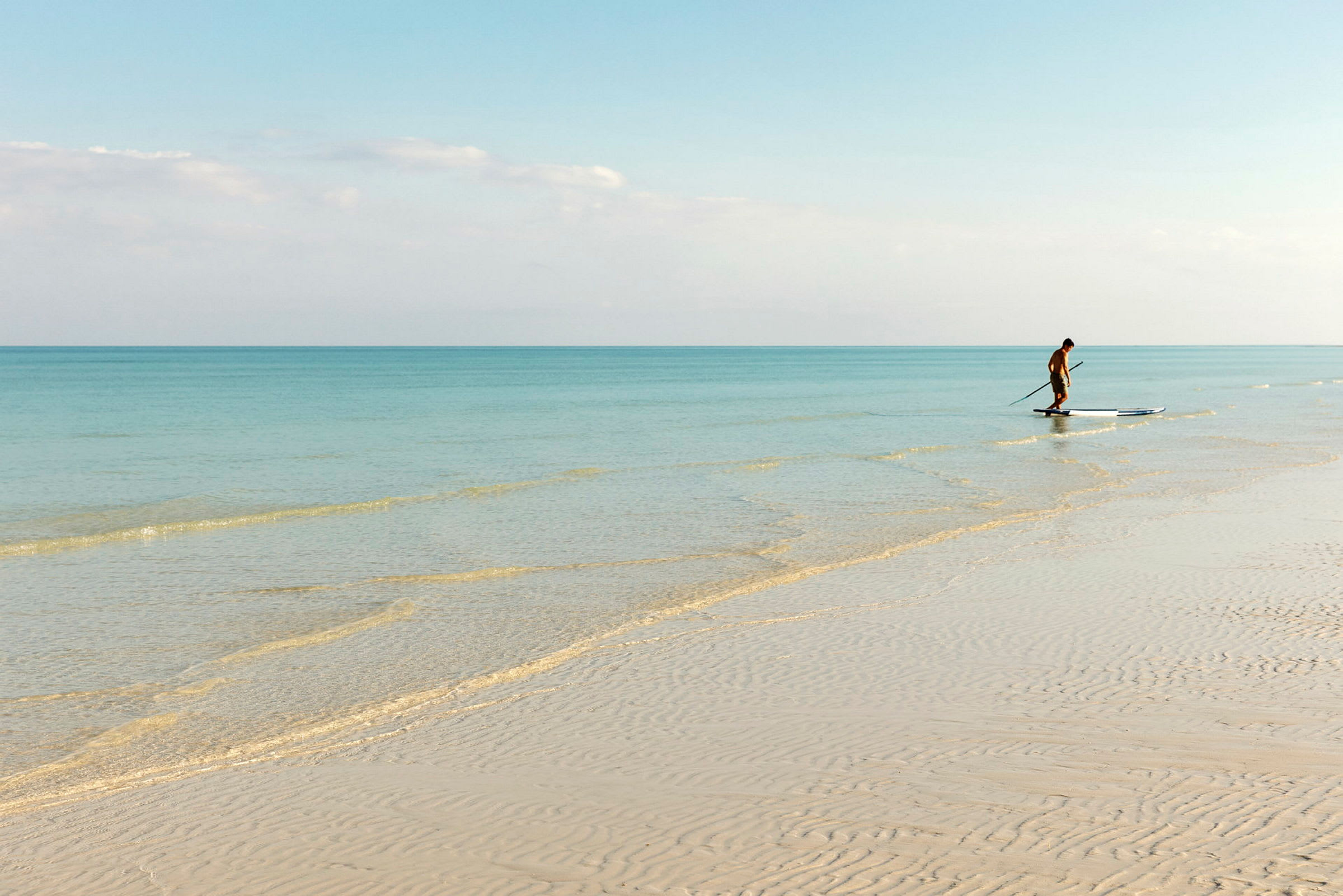 En person ser ud til at stå og paddle på et paddleboard over klart vand ved stranden. (AI-genereret tekst)