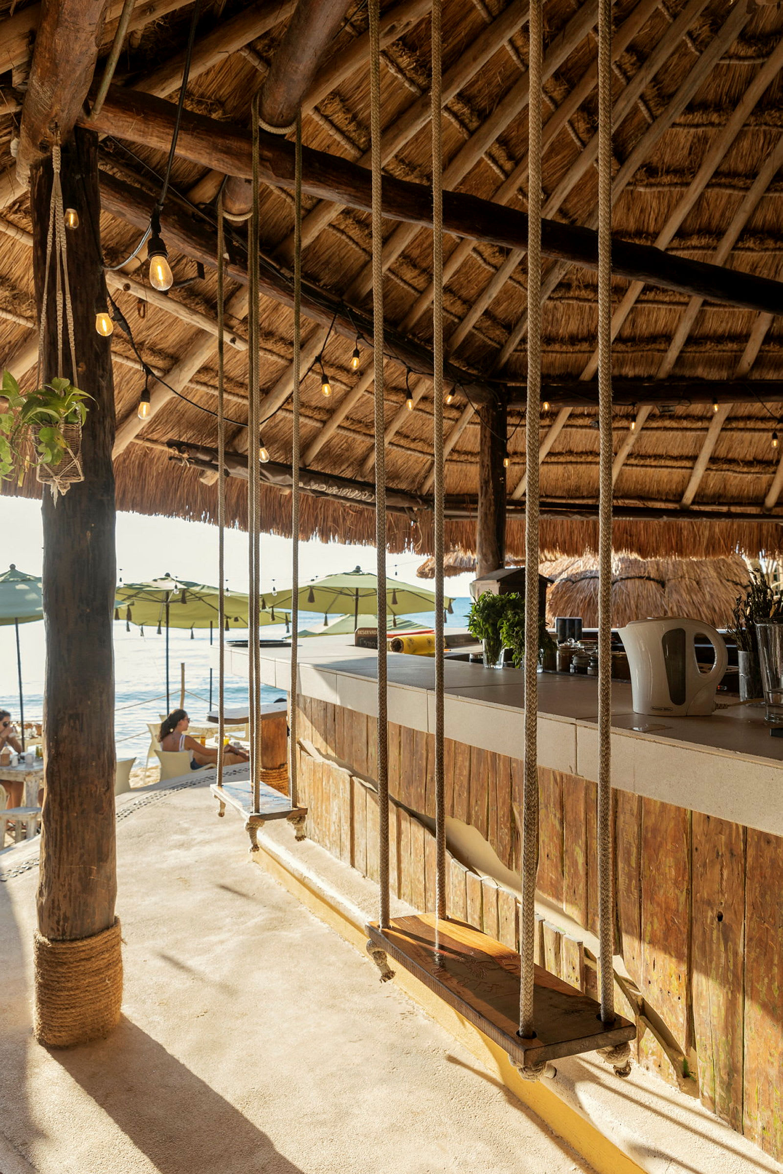 Interiør af en strandbar med gynger ved bardisken og stråtag. (AI-genereret tekst)
