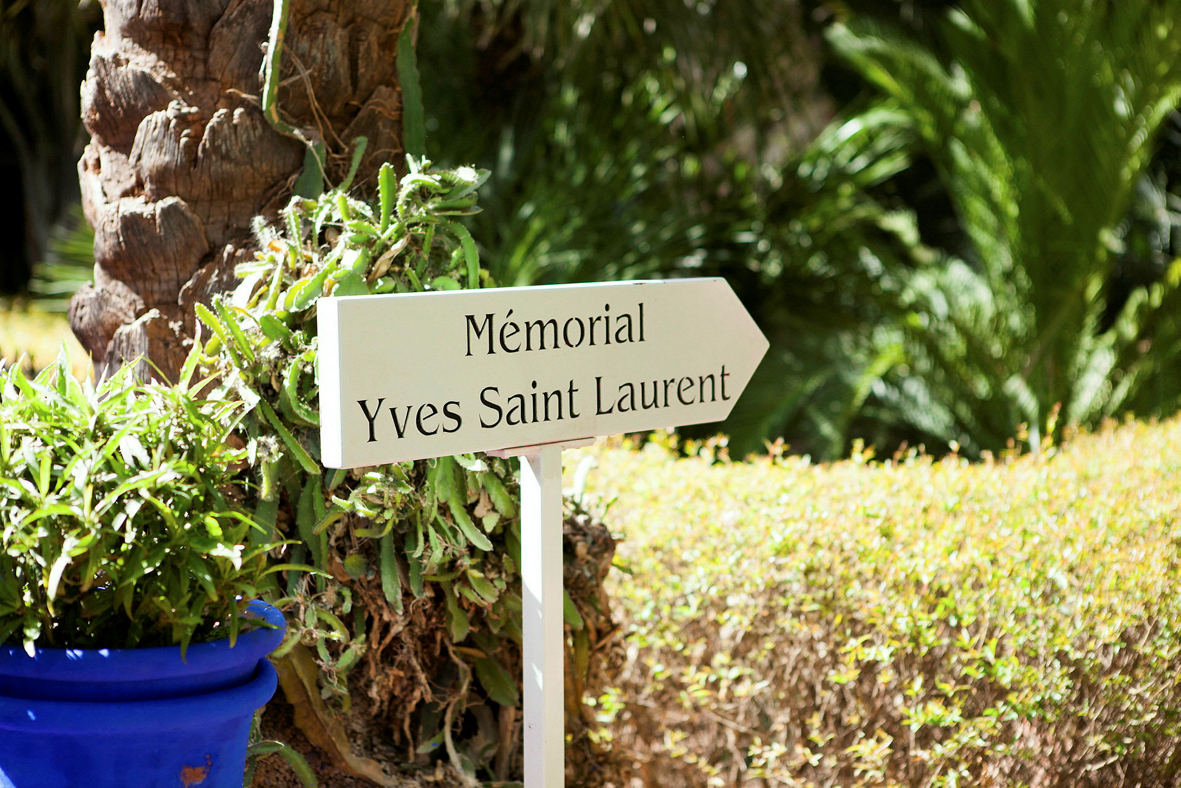 Et skilt med teksten 'Mémorial Yves Saint Laurent' i en have med grønt. (AI-genereret tekst)