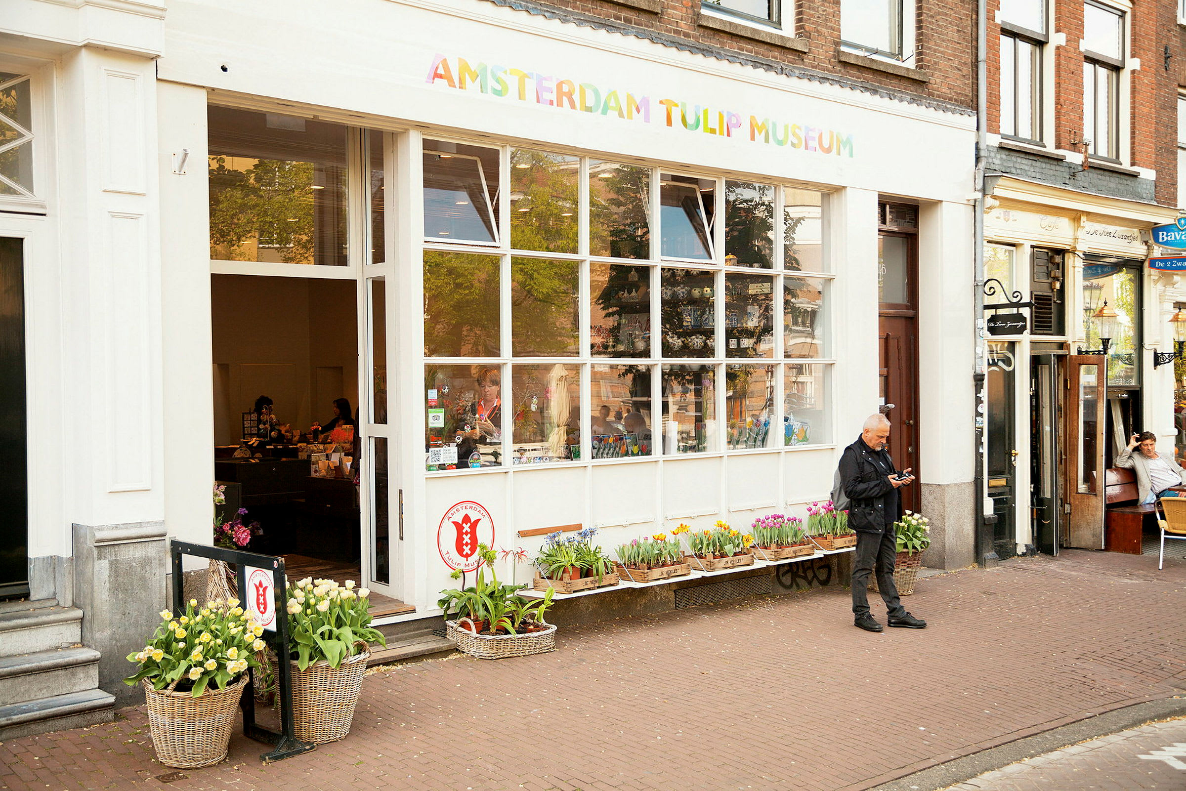 Indgangen til Amsterdam Tulip Museum, med blomster foran og mennesker inde i butikken. (AI-genereret tekst)