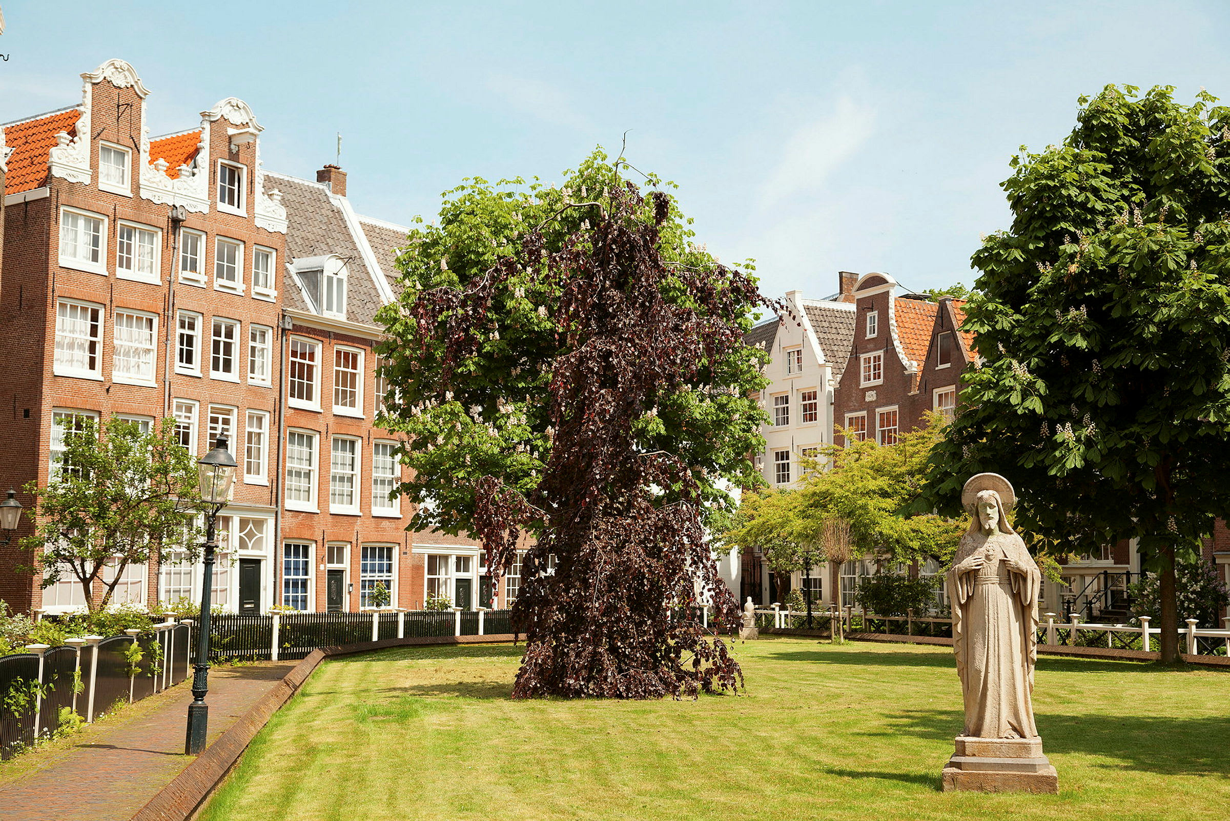 En indre gårdhave med grøntområde, en statue, træer og traditionelle teglhuse i baggrunden. (AI-genereret tekst)