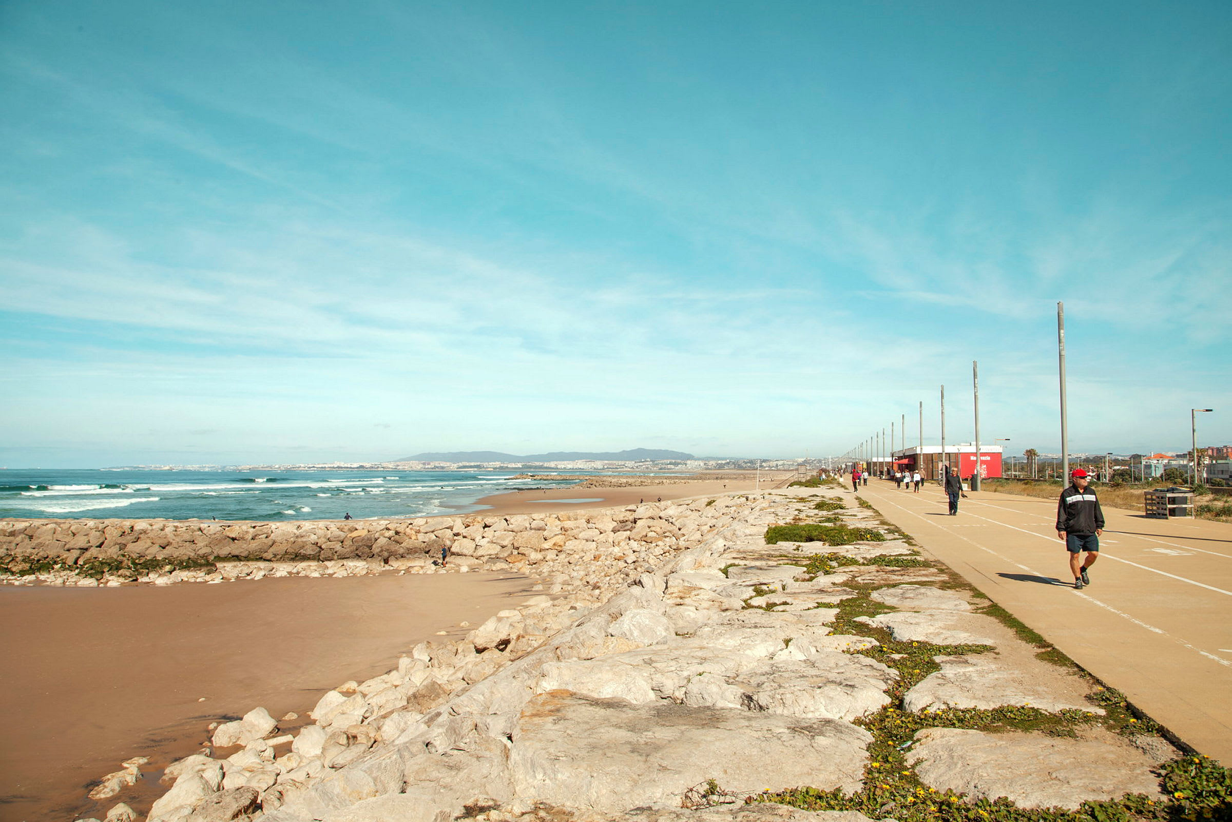 En strandpromenade med en gangsti ved siden af havet og klipper, folk går tur. (AI-genereret tekst)