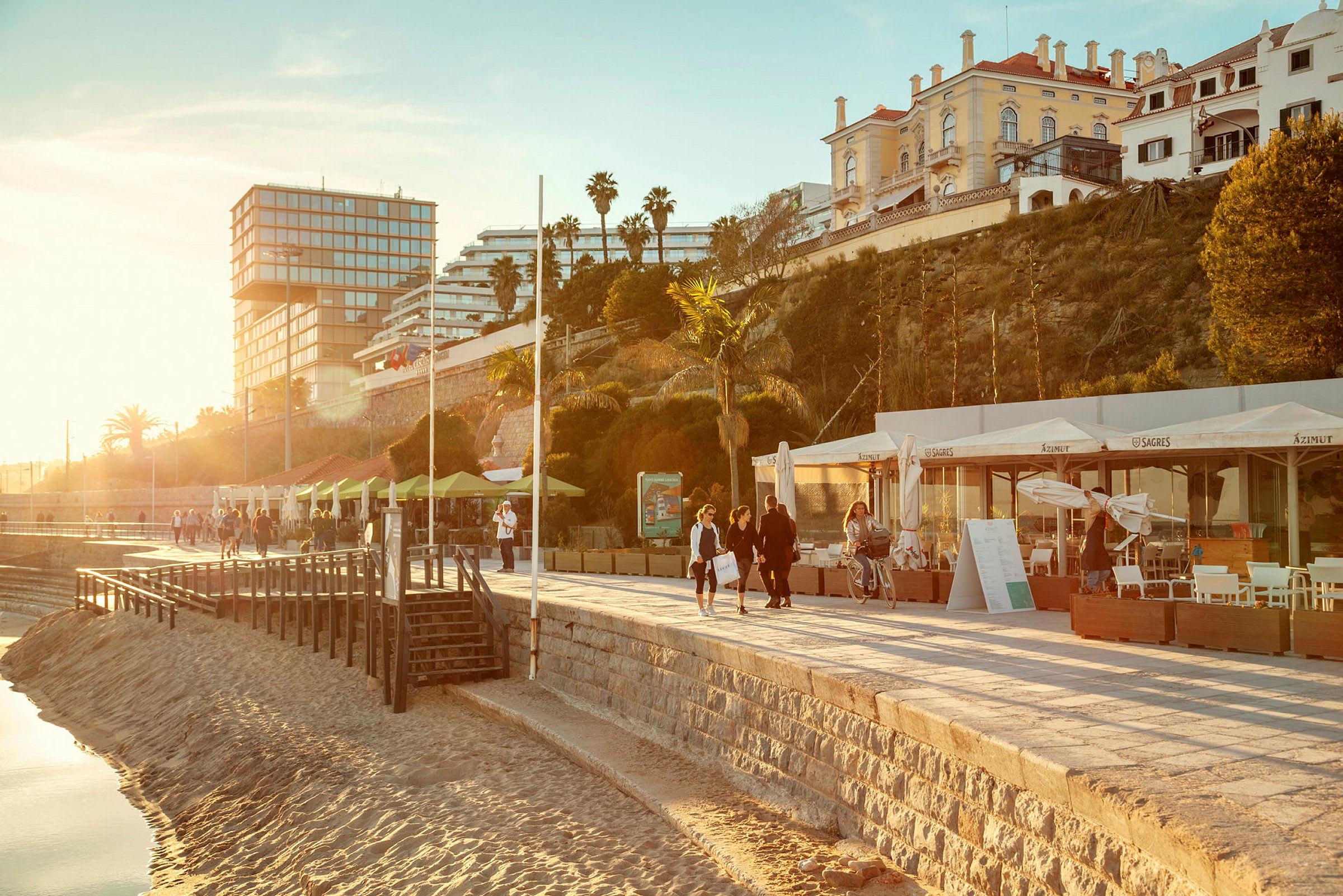 Strandpromenade med bygninger i baggrunden og mennesker, der går tur. (AI-genereret tekst)