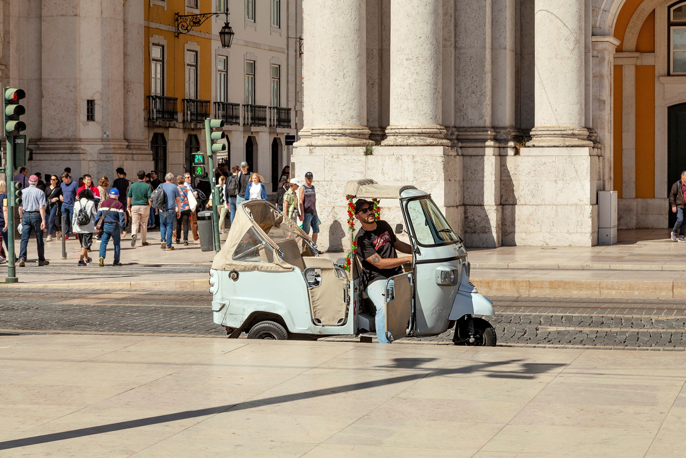 En trehjulet scooter er parkeret foran en bygning med mennesker i baggrunden. (AI-genereret tekst)