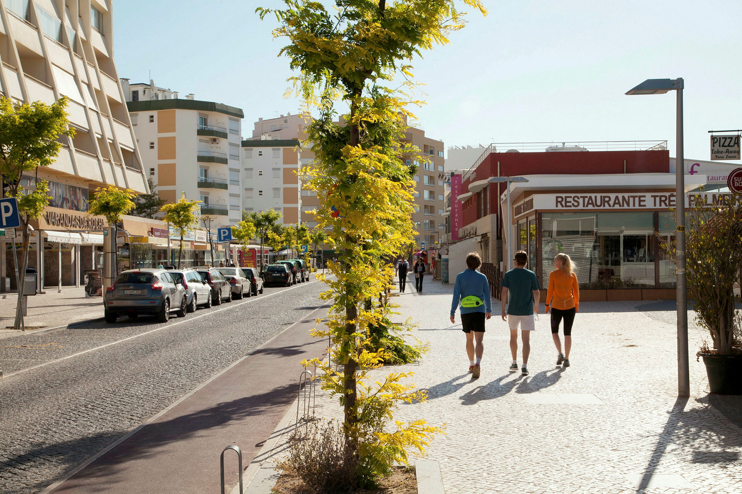 Personer går på en gade med parkerede biler og bygninger i baggrunden. (AI-genereret tekst)