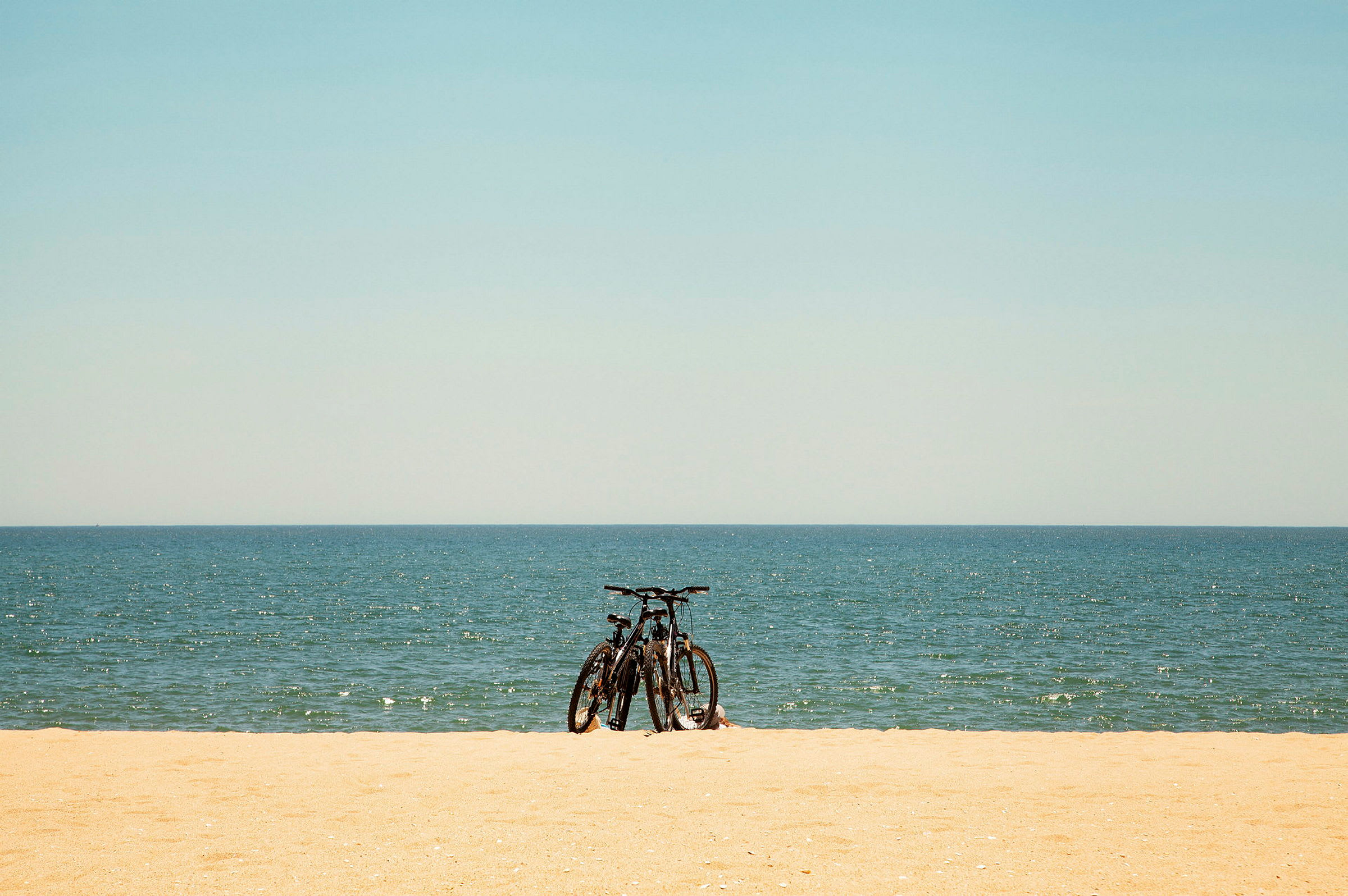 To cykler står på en sandstrand med havet i baggrunden. (AI-genereret tekst)
