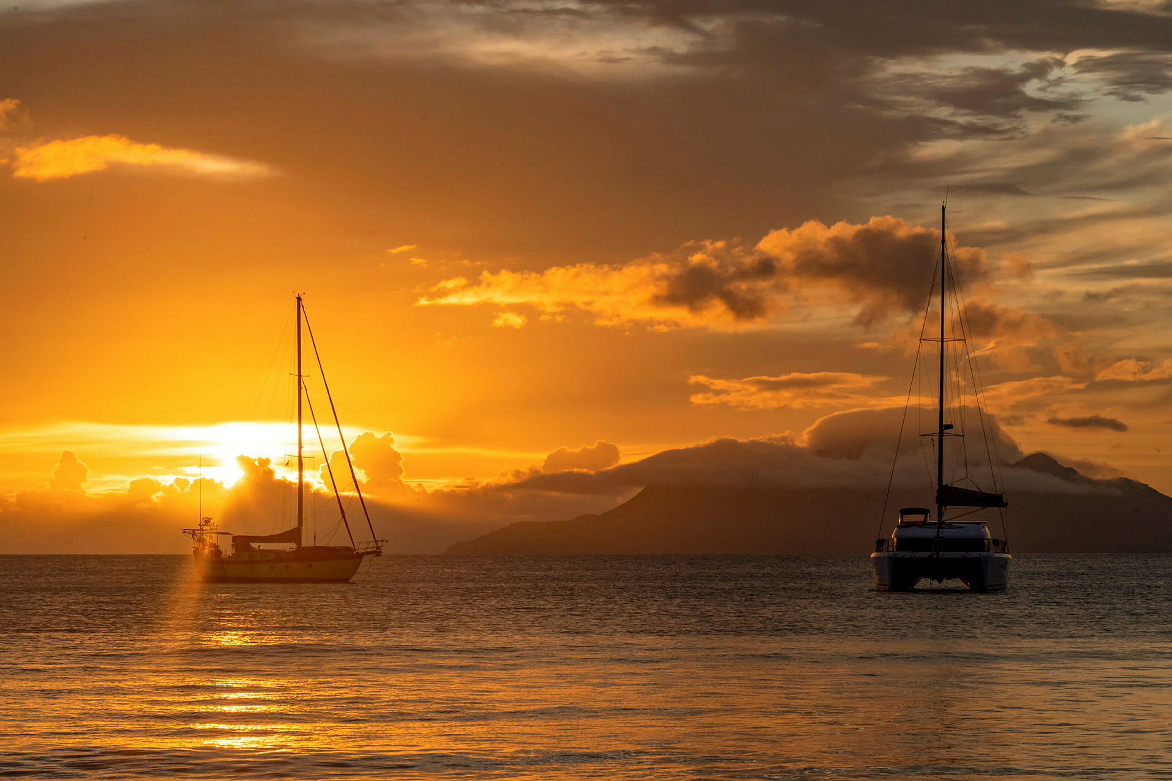 To sejlbåde ligger fortøjet ved havet under en solnedgang, hvor himlen er fyldt med gyldne og orange nuancer. (AI-genereret tekst)