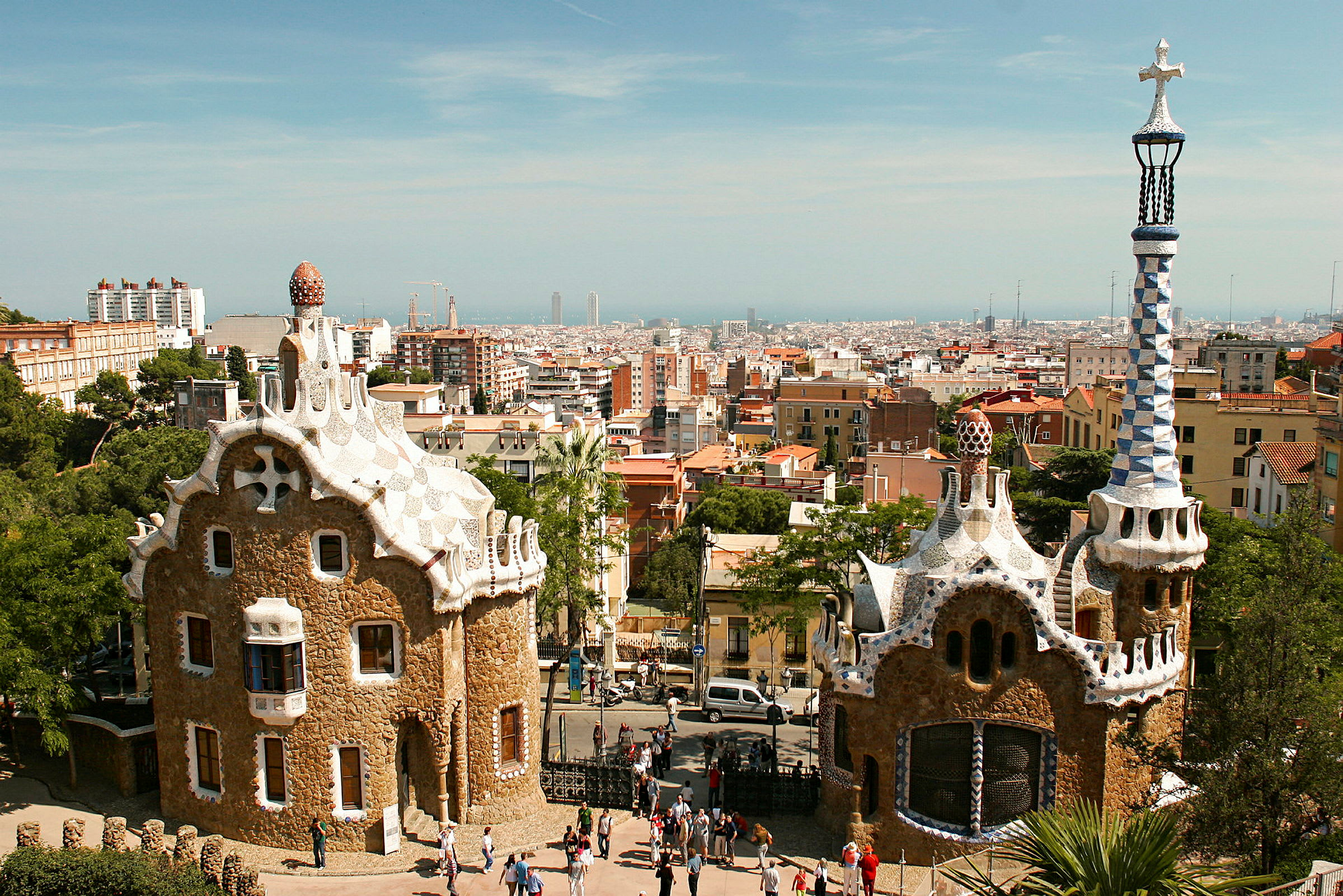 Billede af to unikke bygninger i Park Güell, Barcelona, med byen i baggrunden. (AI-genereret tekst)