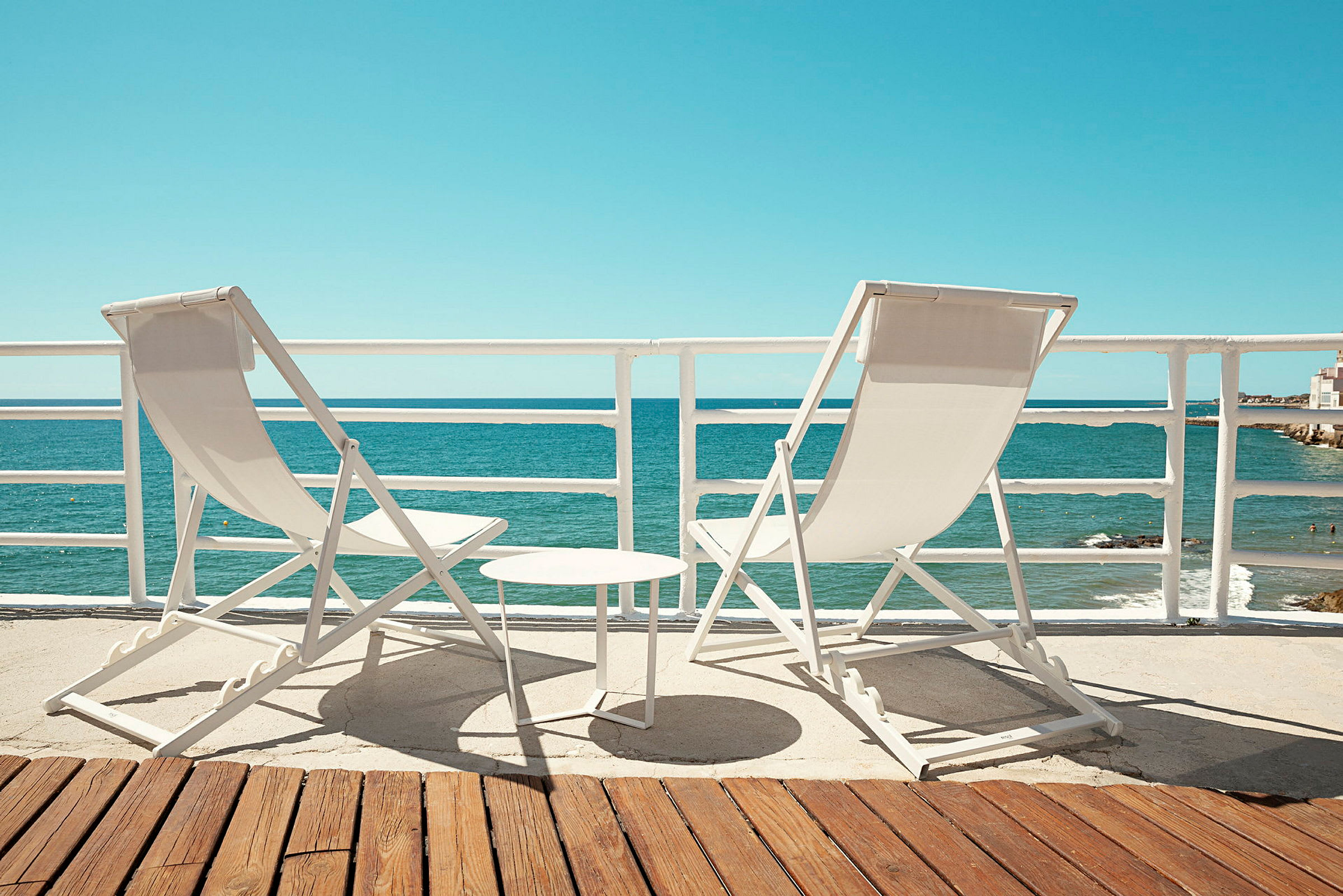 To liggestole og et lille bord står på en terrasse med udsigt over havet. (AI-genereret tekst)