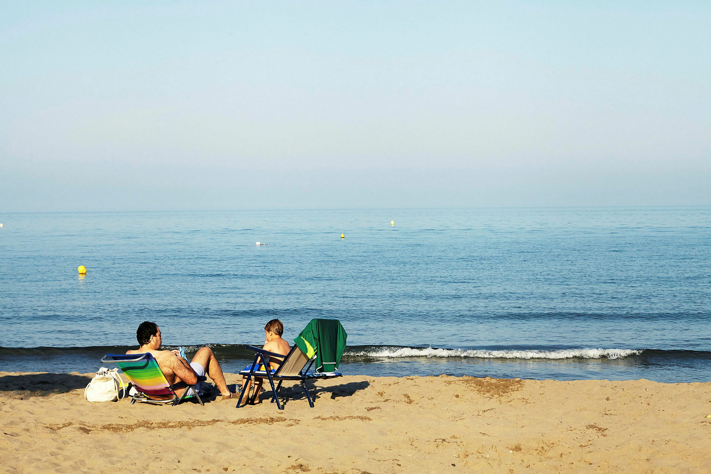 To personer sidder i strandstole på en sandstrand og kigger ud over havet. (AI-genereret tekst)