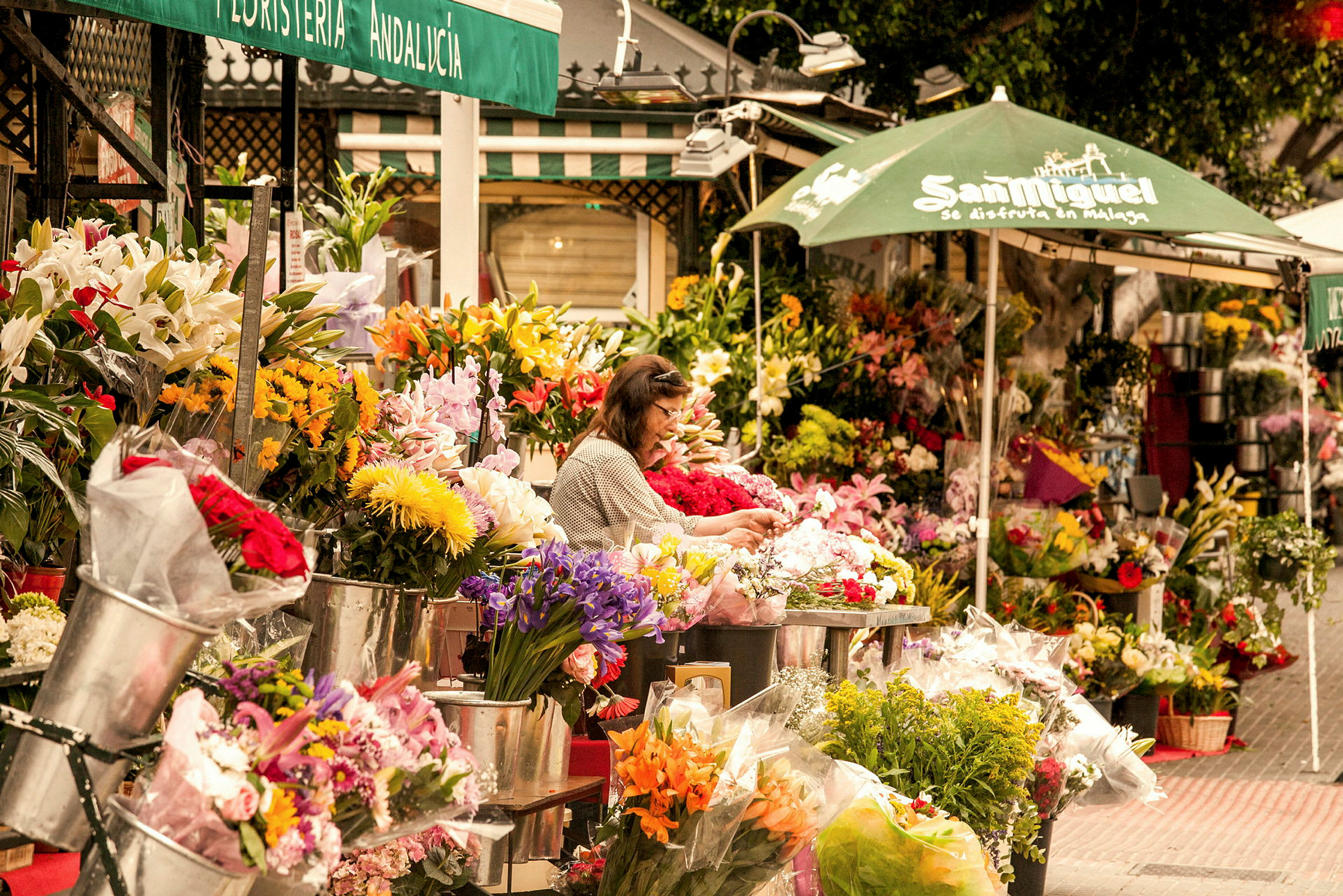 Blomsterbod på en gade med forskellige farverige buketter og arrangementer, samt en person der forbereder blomster. (AI-genereret tekst)