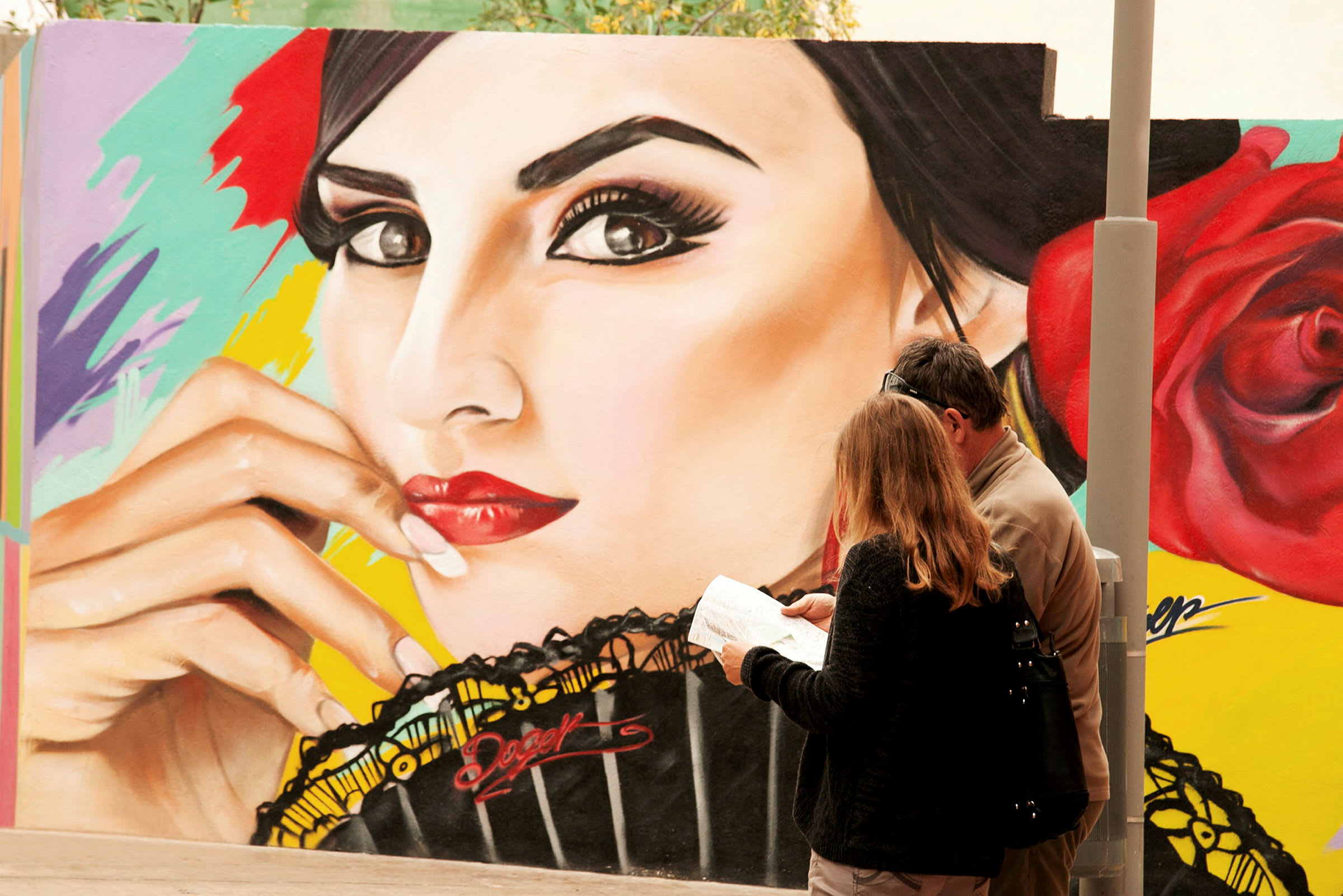 To personer står foran en væg med farverig graffitikunst, der viser et ansigt og en rose. (AI-genereret tekst)
