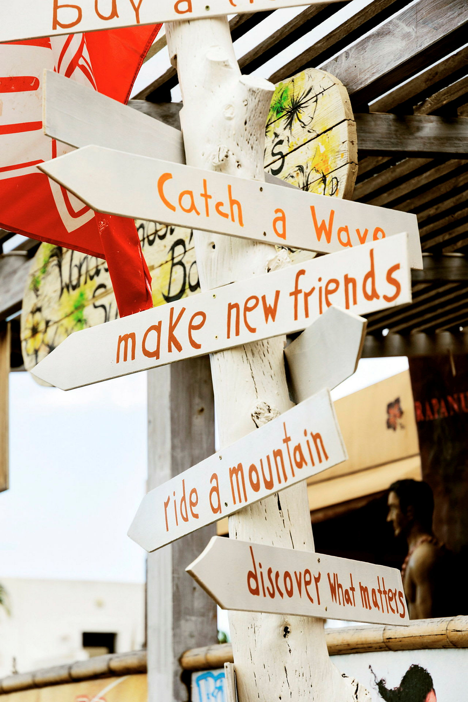 Et træskilt med flere pile, der peger i forskellige retninger, og tekster som "Catch a Wave", "Make new friends", "Ride a mountain" og "Discover what matters". (AI-genereret tekst)