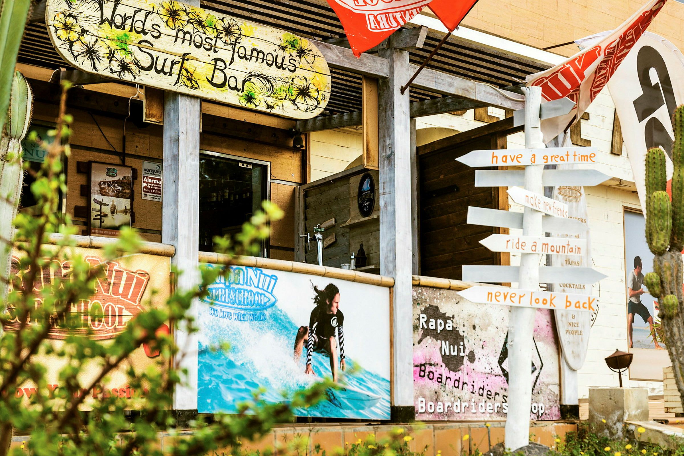 Et surfhotel med farverige skilte og dekorationer, inklusive en figur af en surfer i vandet, og et vejskilt der peger i forskellige retninger. (AI-genereret tekst)