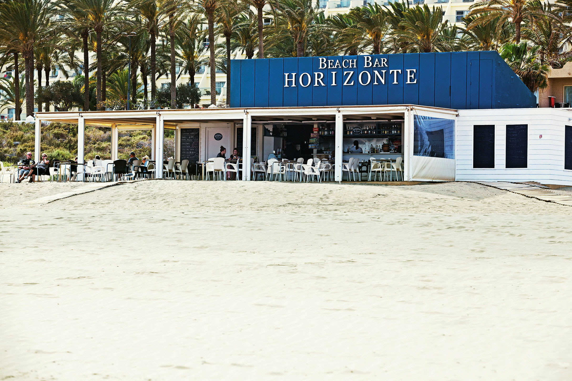 En strandbar med navnet Horizonte, beliggende tæt på en sandstrand og omgivet af palmer. (AI-genereret tekst)