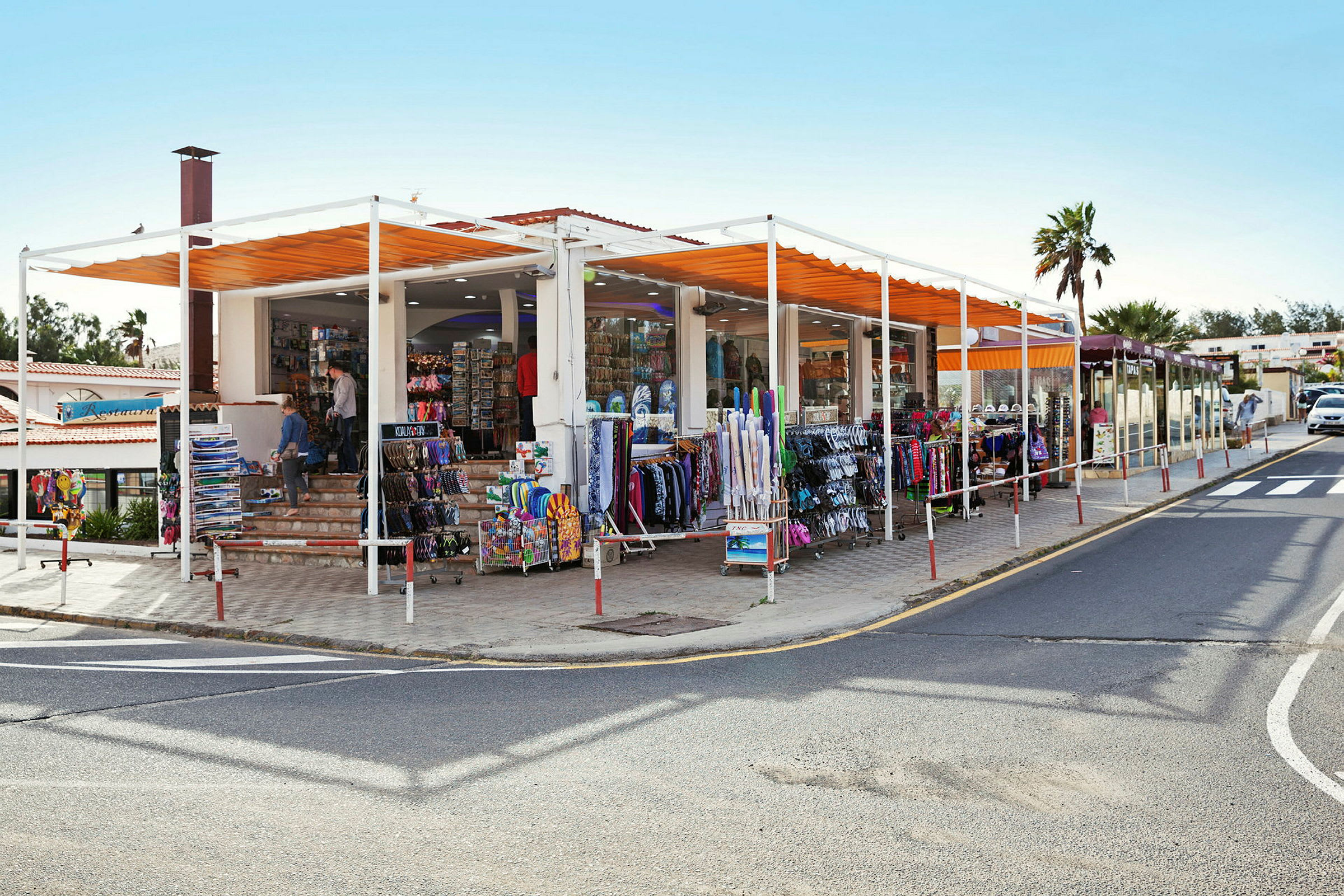 En butik med varer opstillet udenfor, herunder tøjstativer og stativer med souvenirs, beliggende ved siden af en vej. (AI-genereret tekst)
