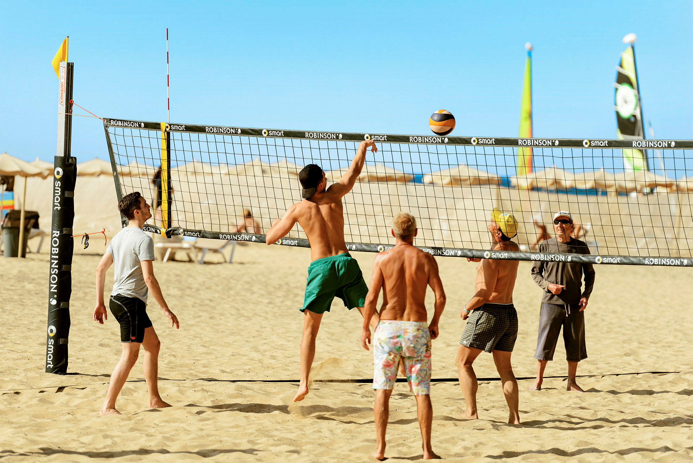 En gruppe mennesker spiller beachvolleyball på en sandstrand under en klar blå himmel. (AI-genereret tekst)
