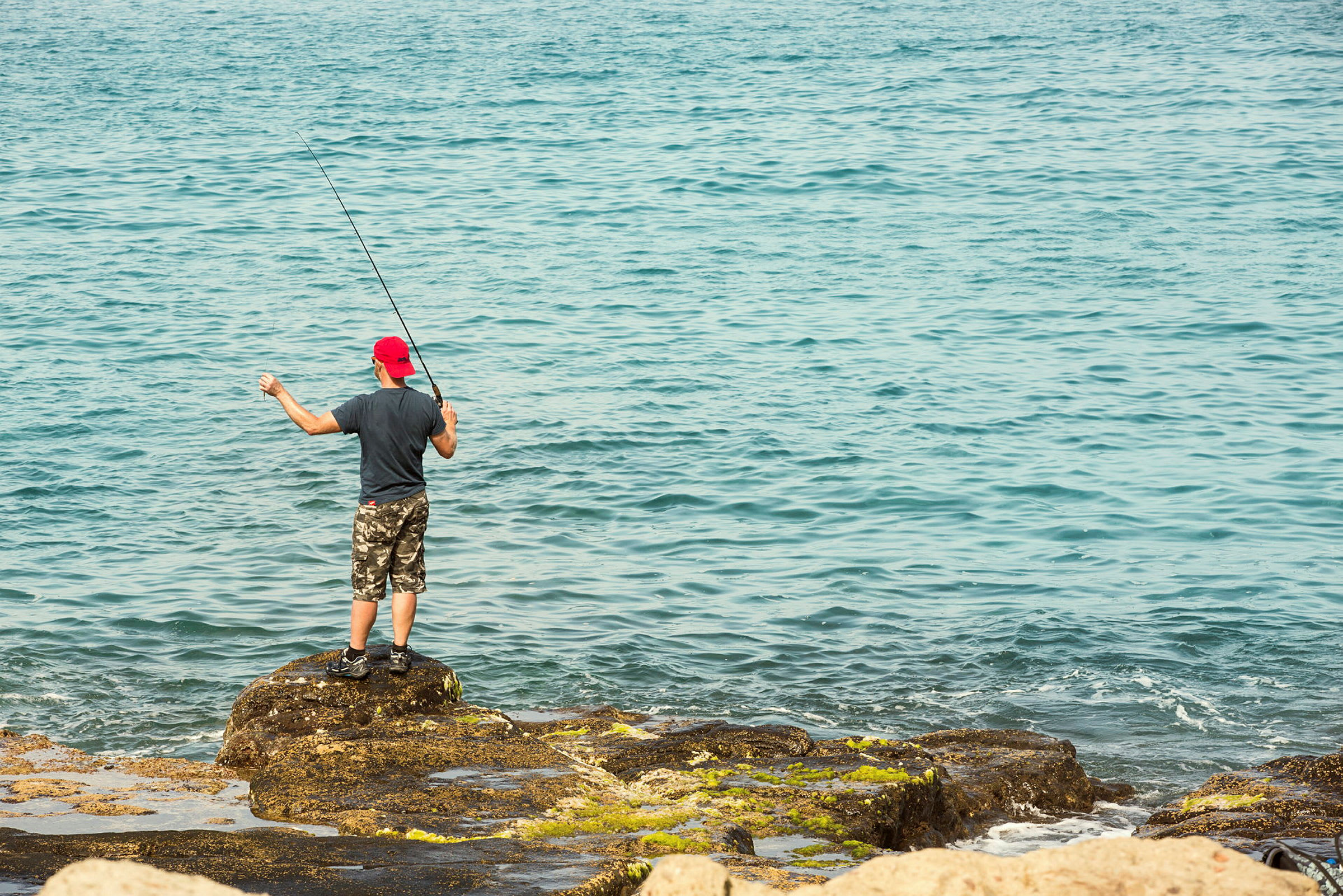 En person fisker ved havet på klipper. (AI-genereret tekst)