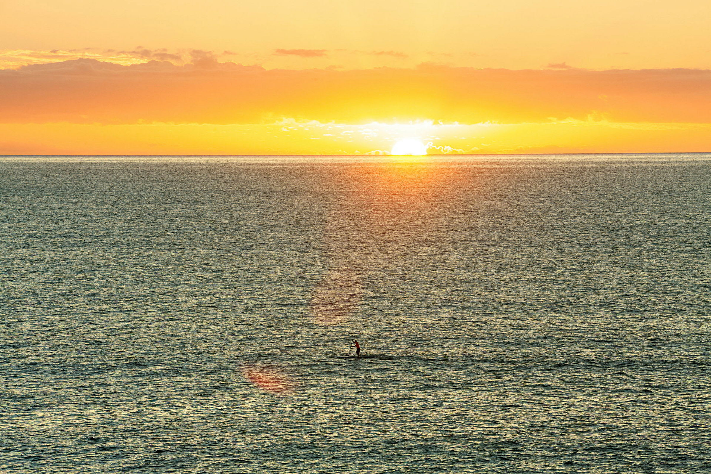 En solnedgang over havet med en person, der står padlende på et bræt. (AI-genereret tekst)