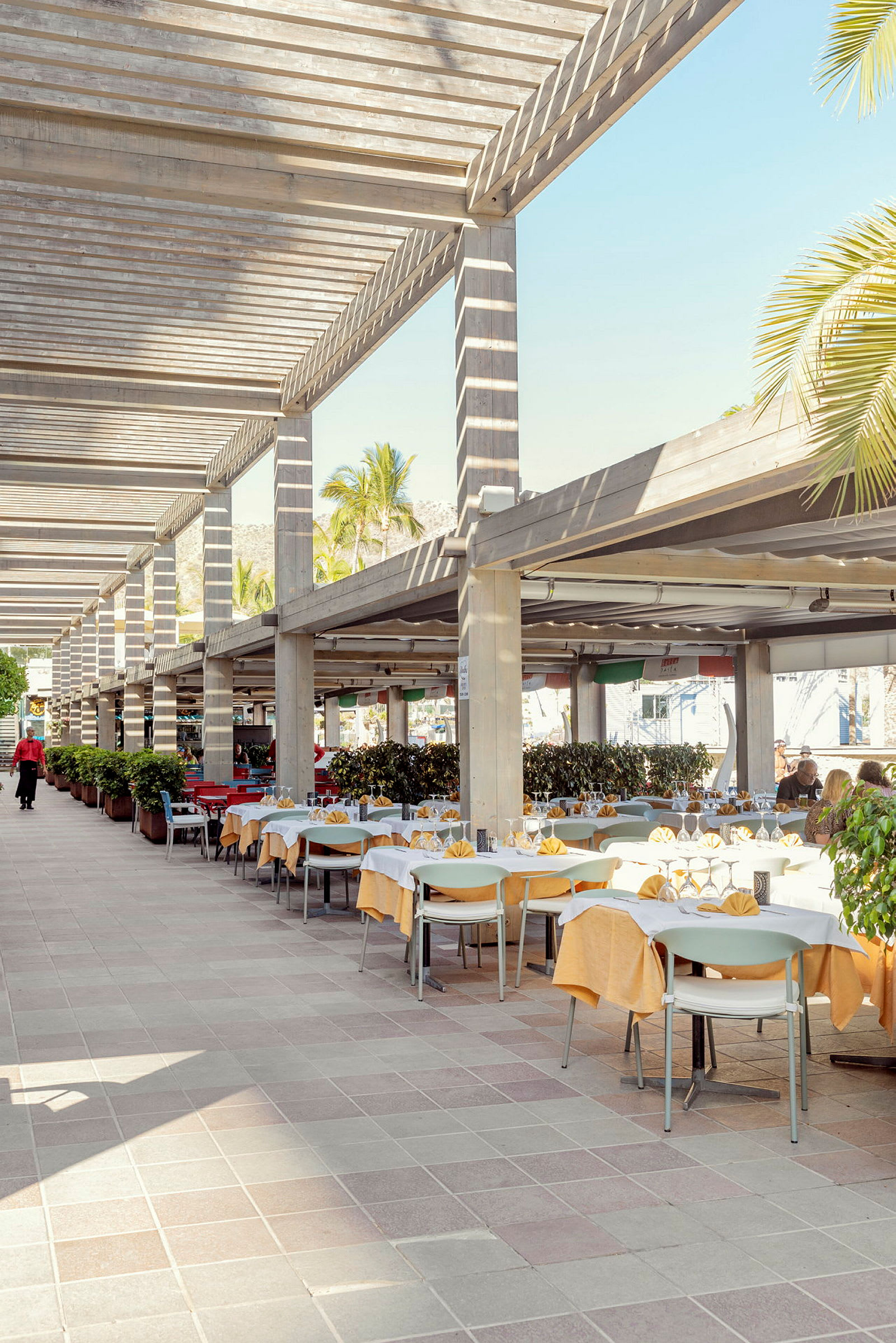 Udendørs serveringsområde med dækkede borde og stole under pergola. (AI-genereret tekst)