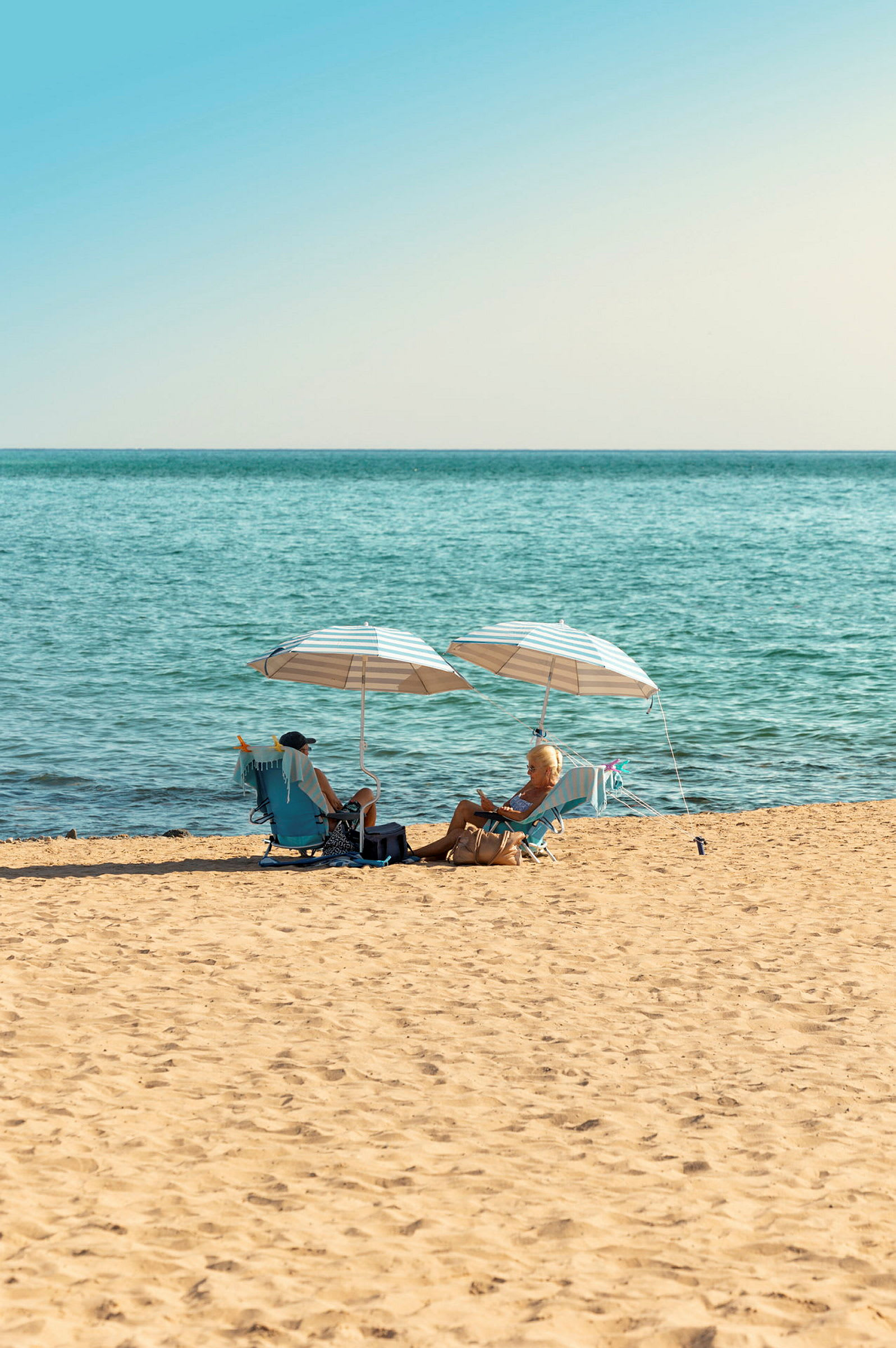 En strand med to personer, der sidder under parasoller og nyder udsigten over havet. (AI-genereret tekst)