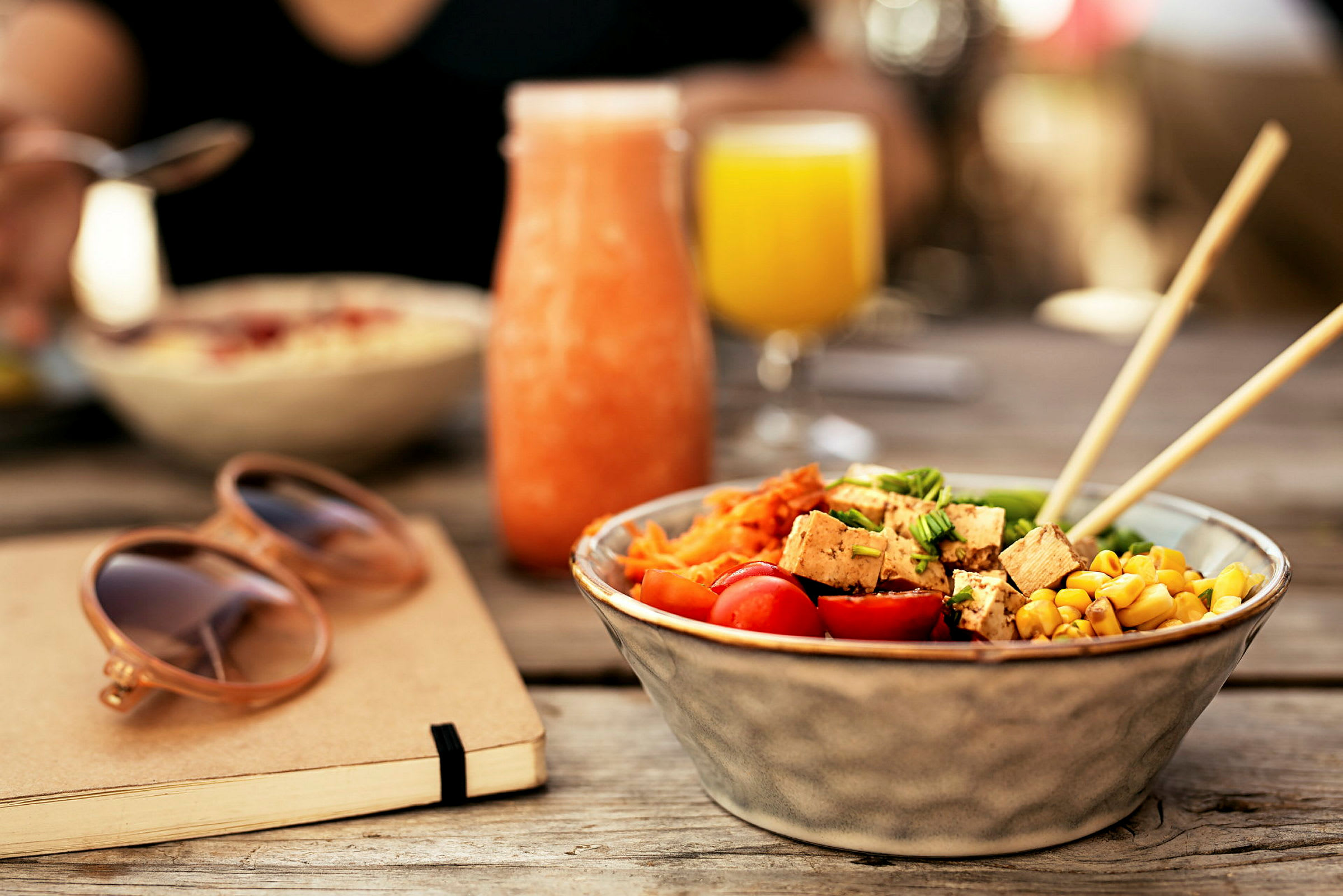 En skål med salat, et glas med orange drik og et glas med gul drik på et bord. (AI-genereret tekst)