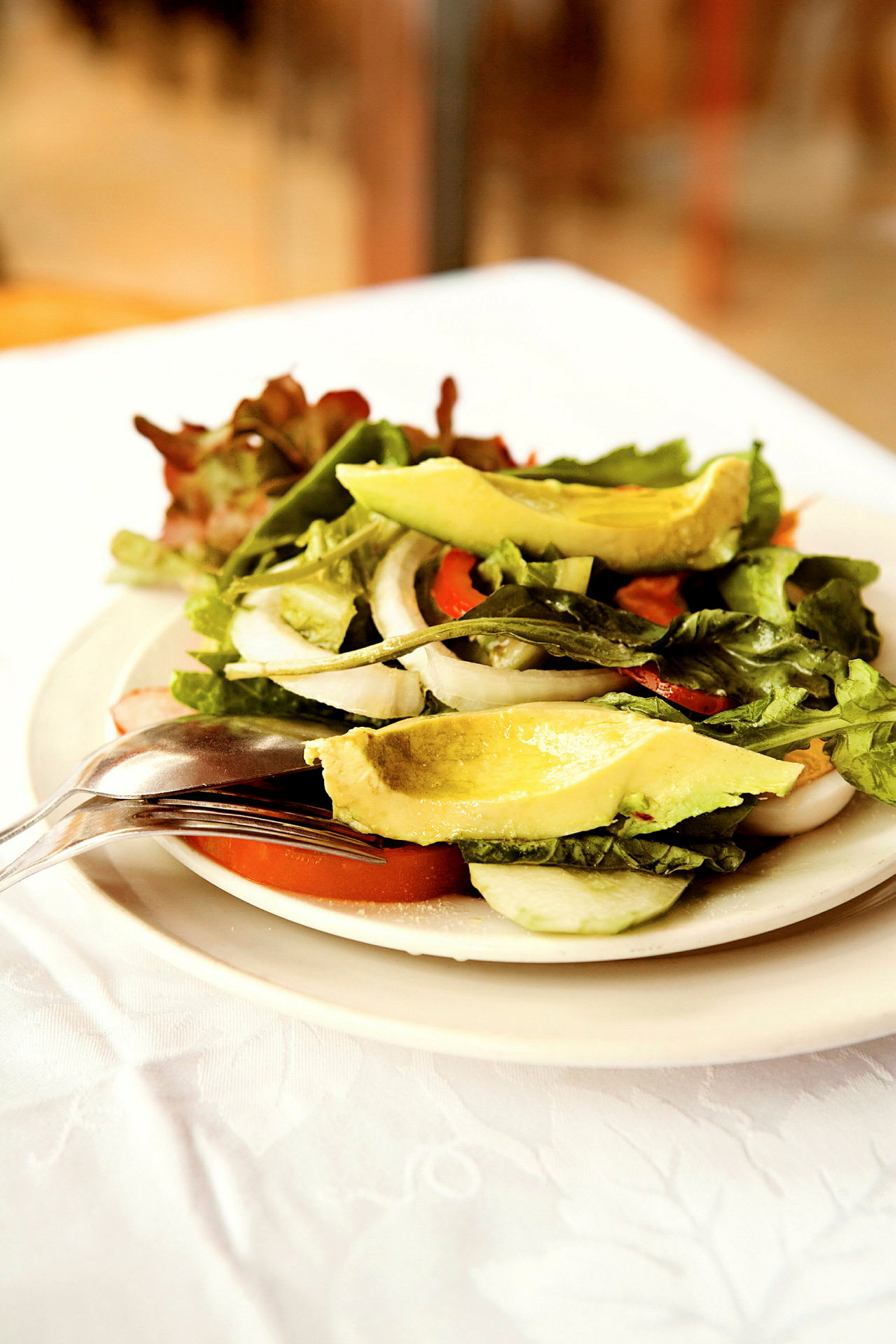 En salat med avocado, tomater, løg og bladsalat serveret på en tallerken. (AI-genereret tekst)