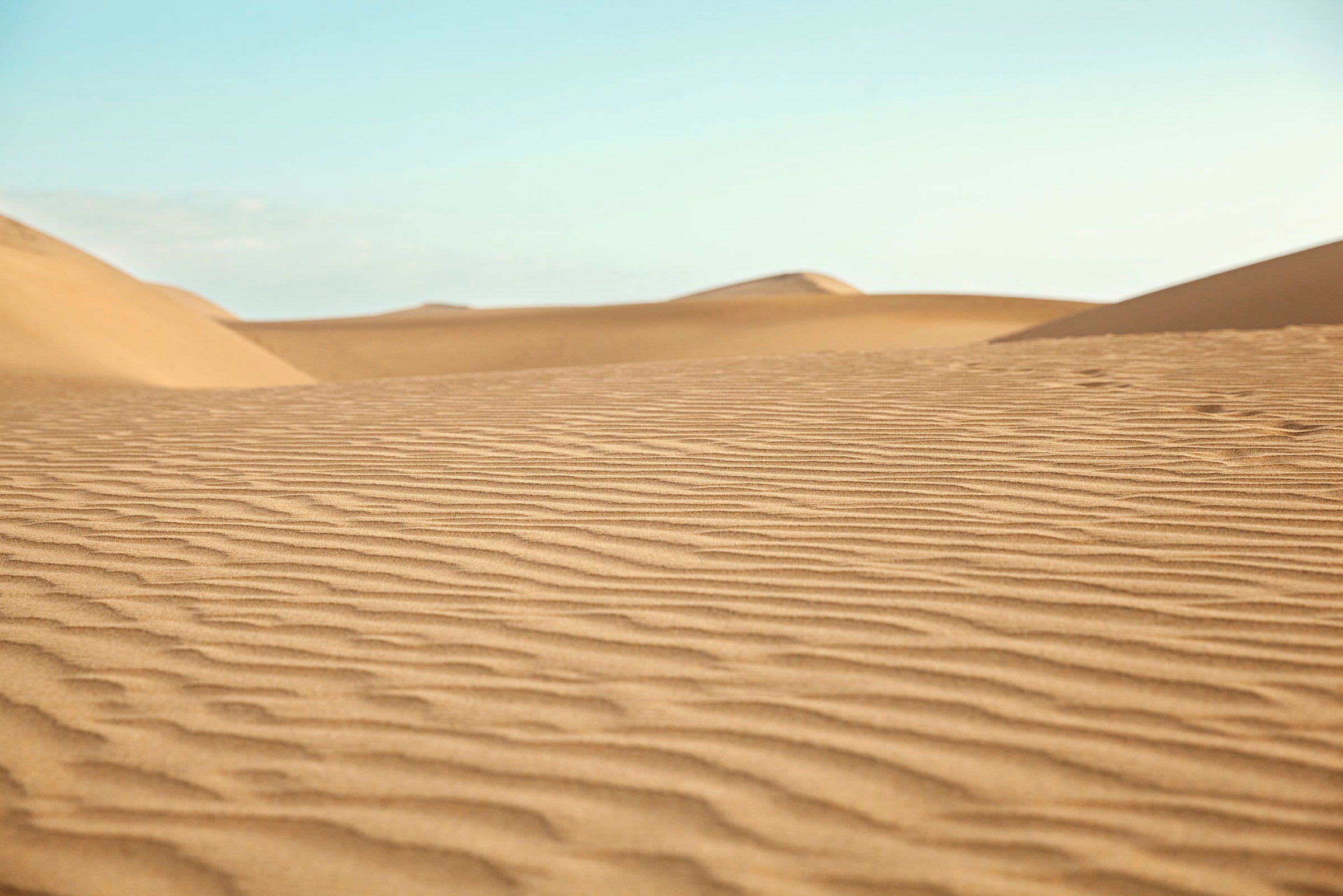 Billede af sandklitter med fint mønstret sand. Klar blå himmel i baggrunden. (AI-genereret tekst)