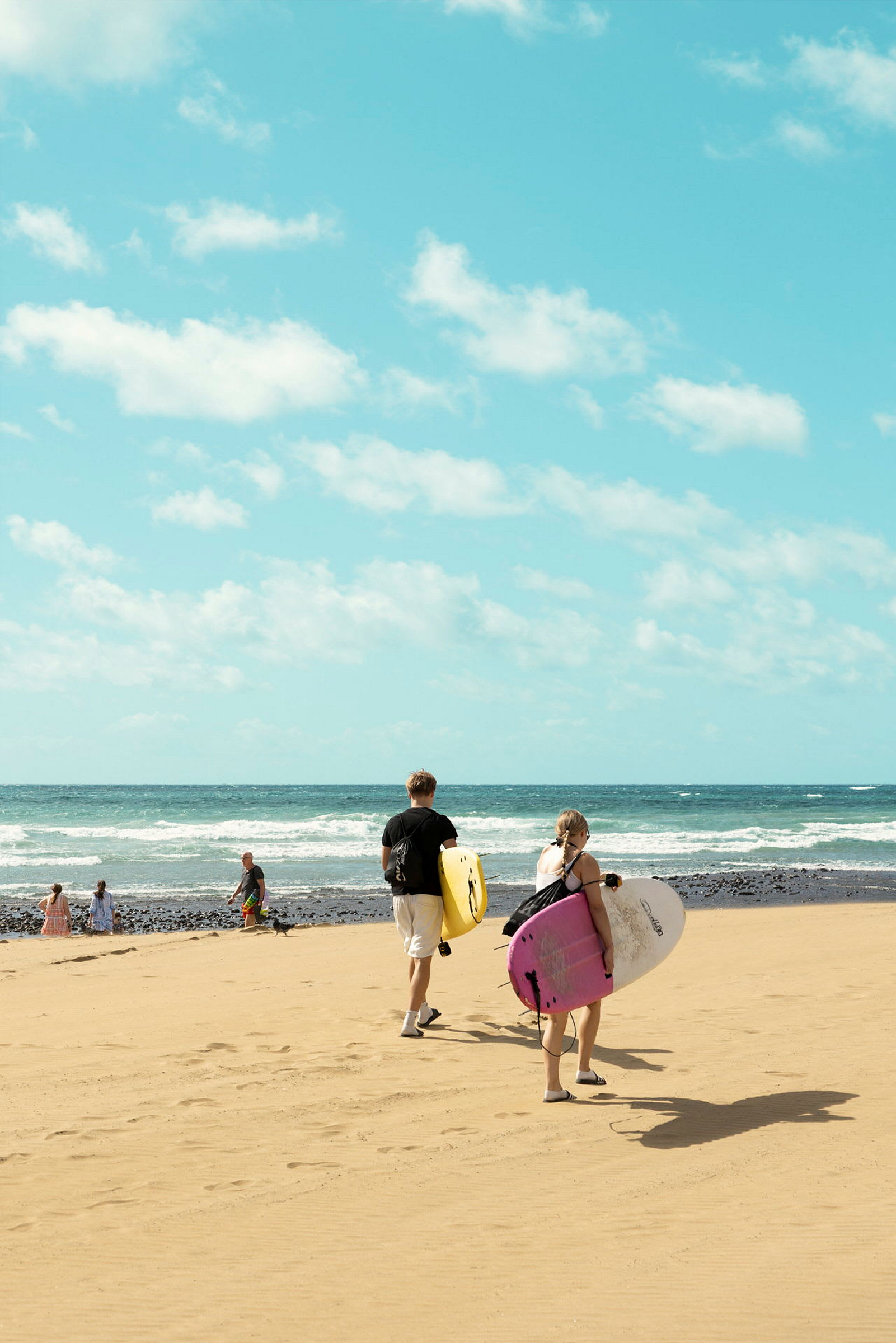 To personer går mod havet på en sandstrand, bærende på surfbrætter. (AI-genereret tekst)