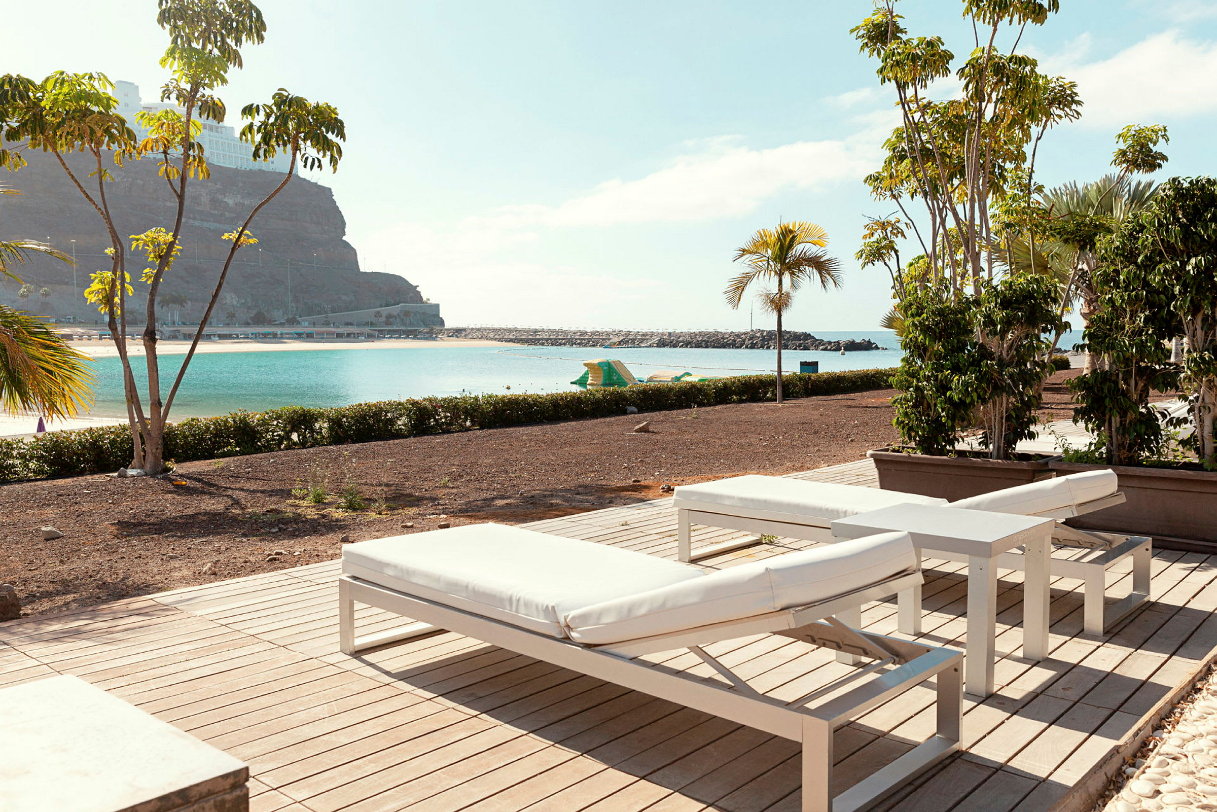 Liggestole på en terrasse med udsigt over en strand og havet. (AI-genereret tekst)