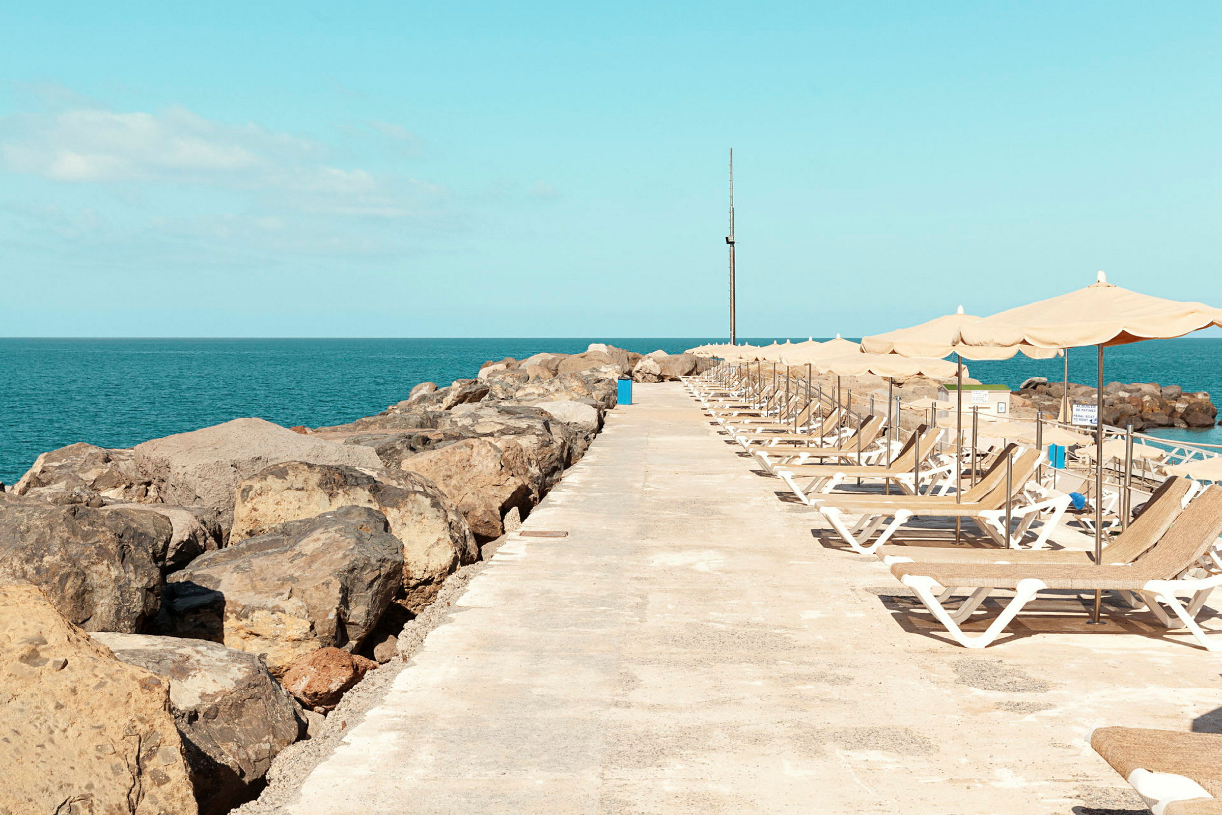 Liggestole og parasoller på en stenstrandpromenade ved havet. (AI-genereret tekst)