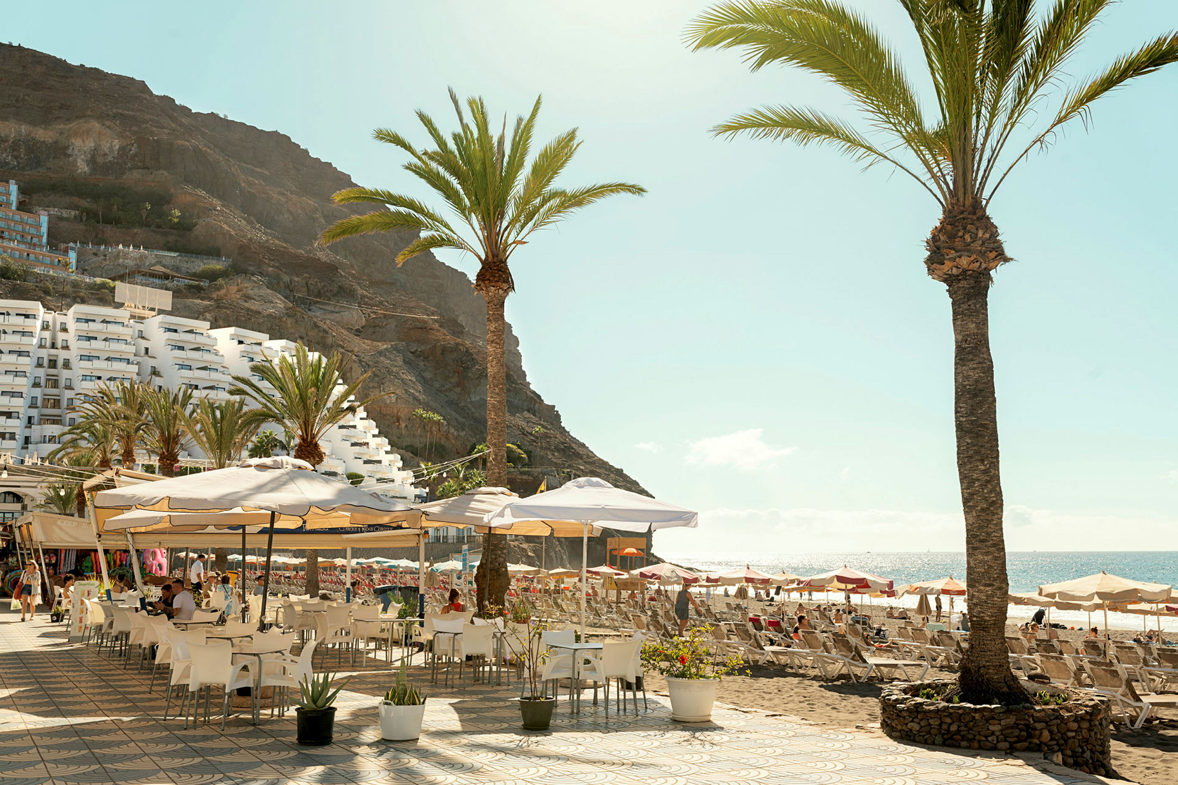 Udendørsrestaurant med parasoller og palmer nær en strand. (AI-genereret tekst)
