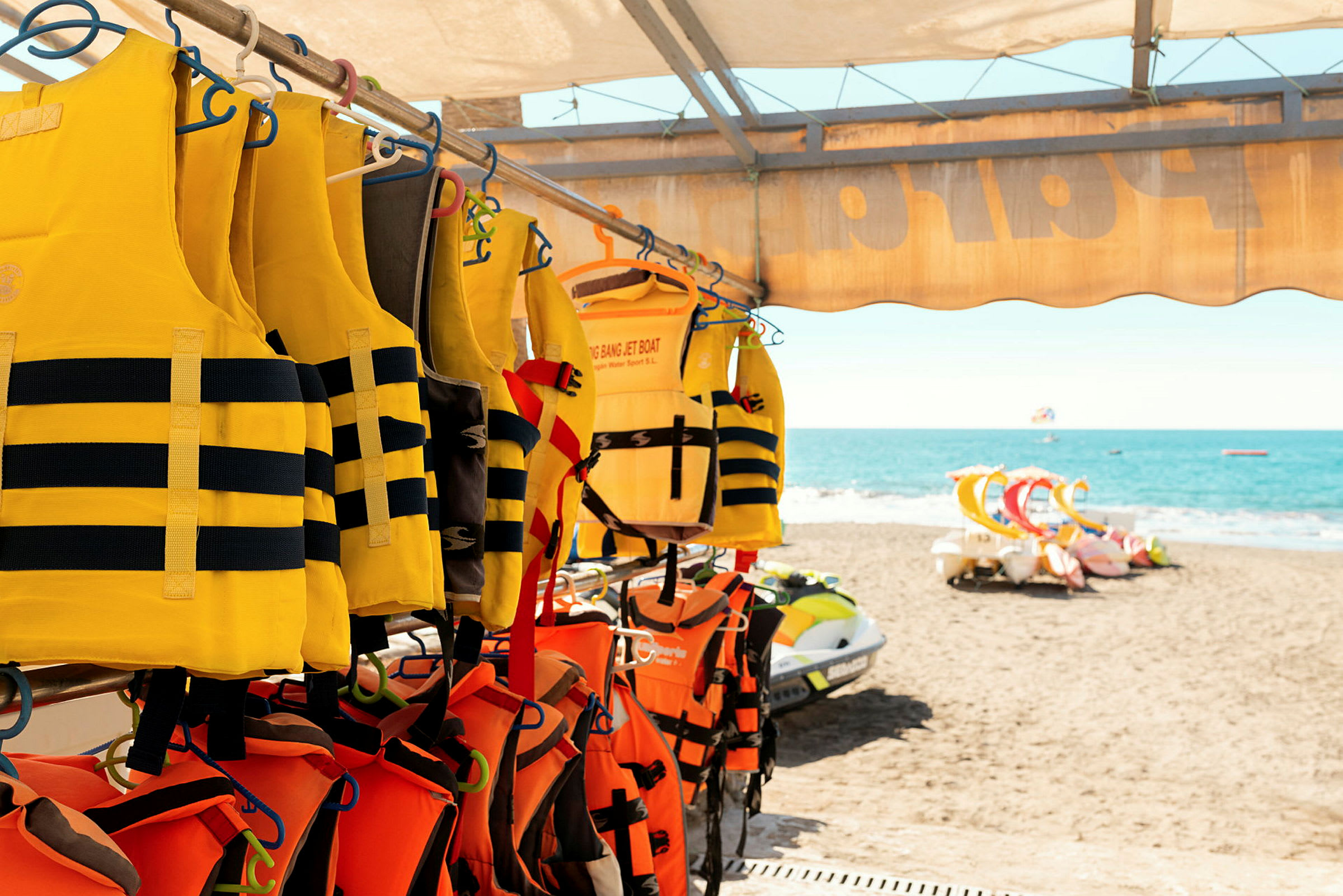 Gule og orange redningsveste hænger på en stang ved en strand med havudsigt. (AI-genereret tekst)