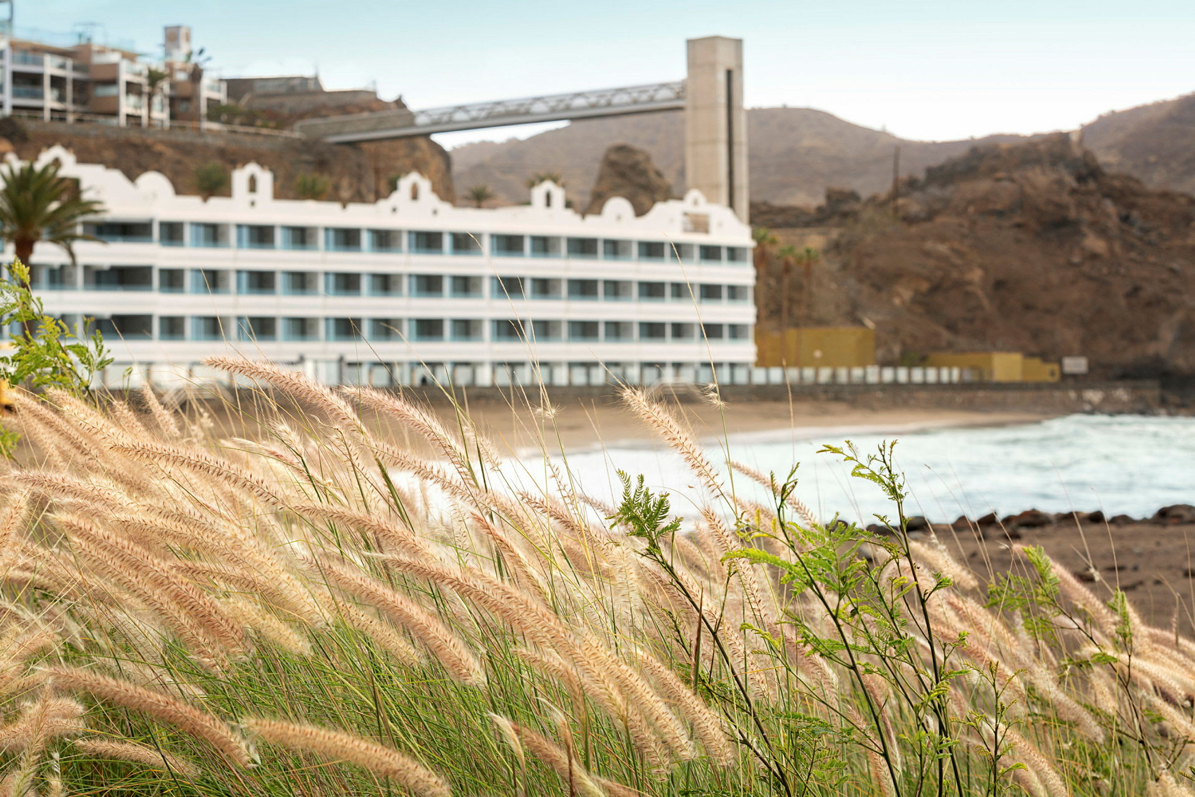 Billede af et hotel ved en klippefyldt strand med græs i forgrunden. (AI-genereret tekst)