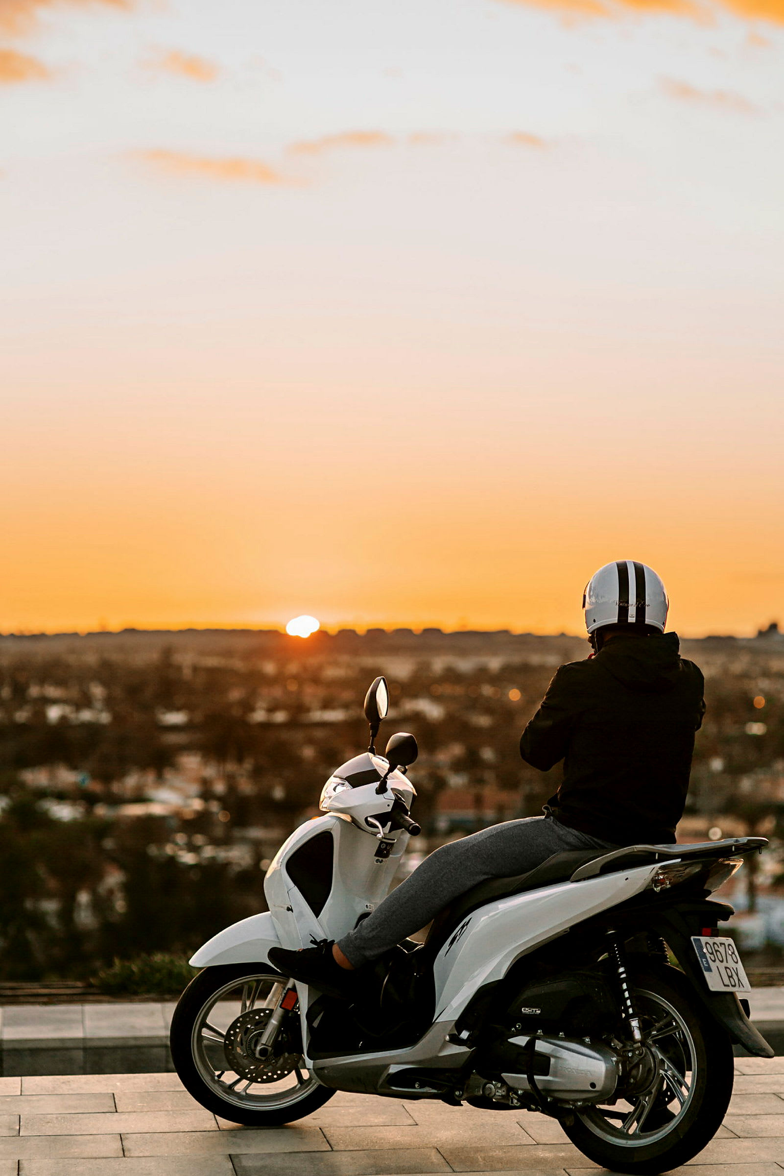 En person sidder på en hvid scooter og ser på solnedgangen. (AI-genereret tekst)