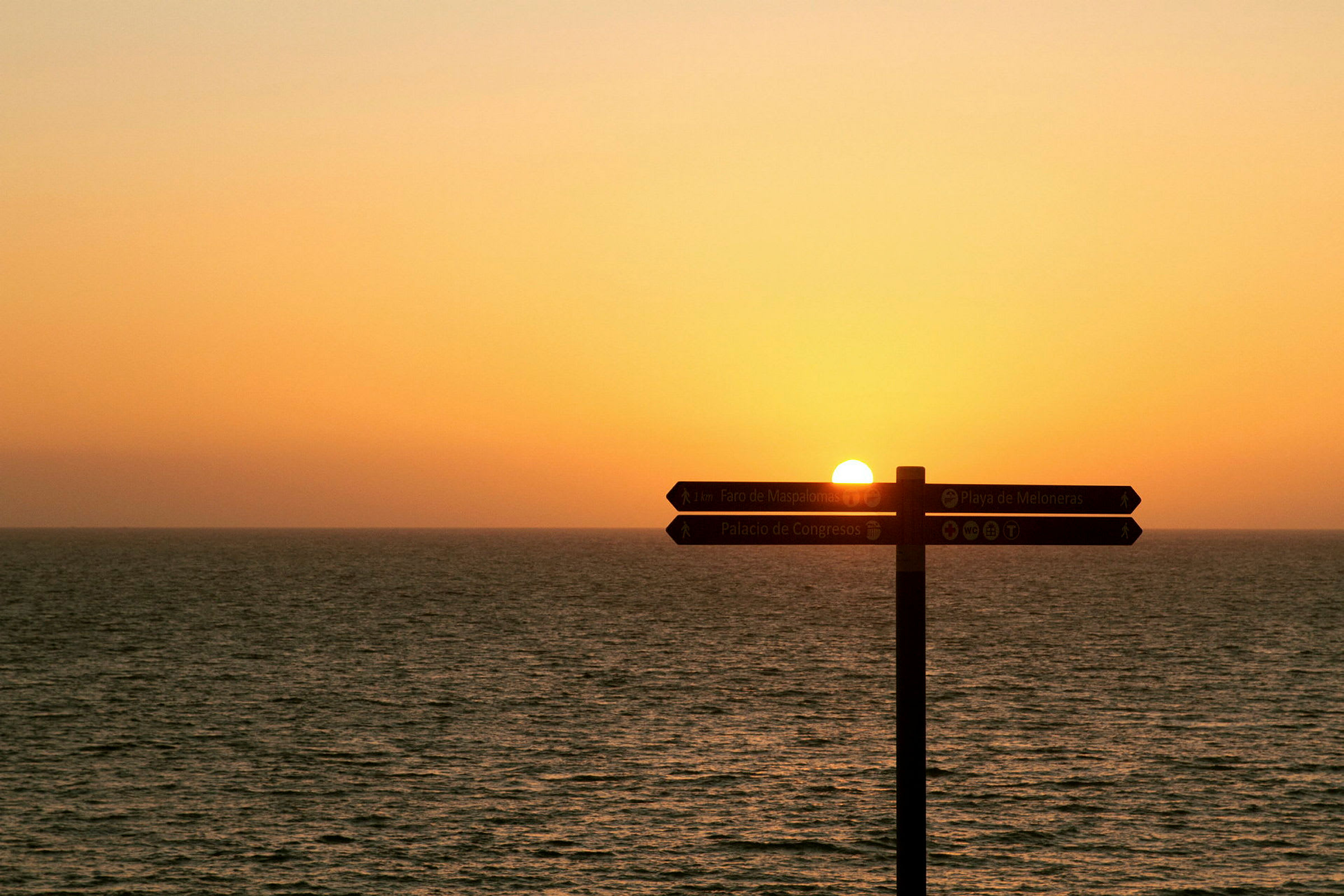 Solnedgang over havet med et vejskilt. (AI-genereret tekst)