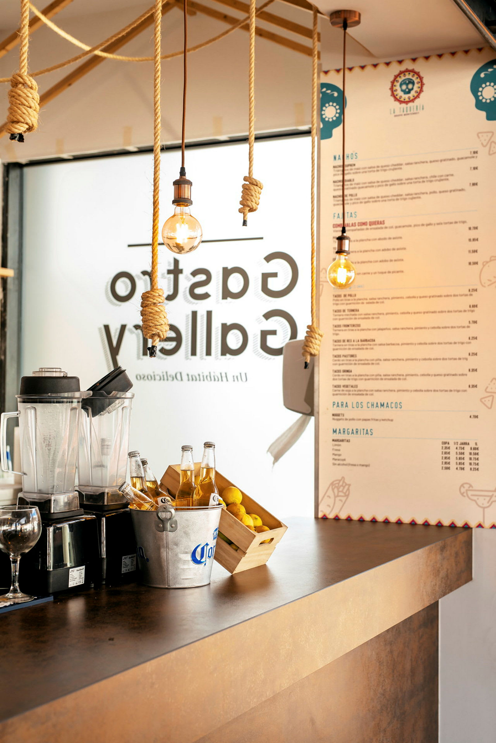 Disk i en restaurant med blender, ølspand, citroner og menu på væggen. (AI-genereret tekst)