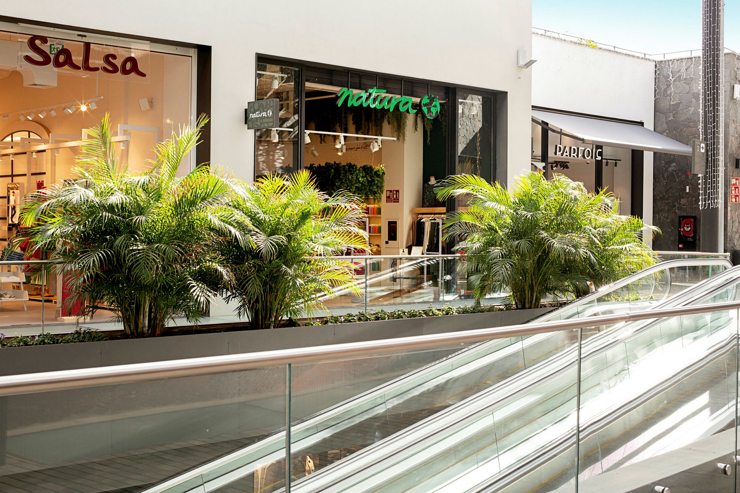 Et shoppingcenter med butikker, planter og rulletrapper. (AI-genereret tekst)